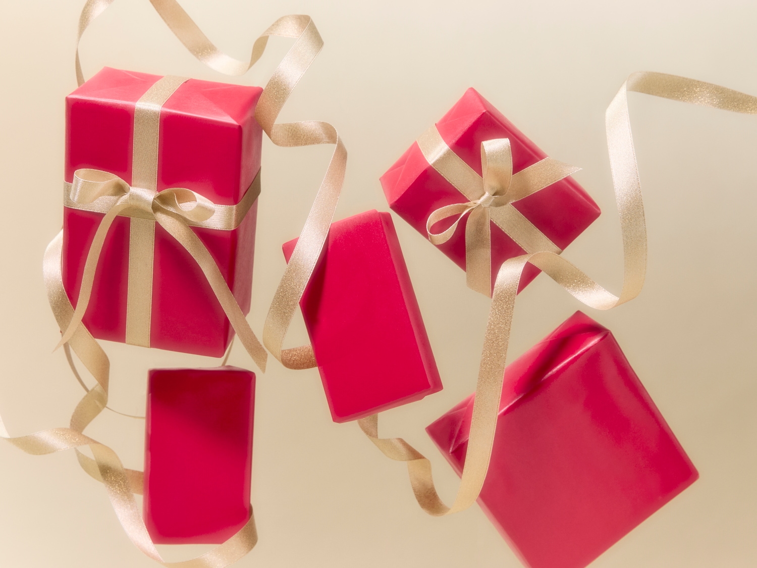 Une collection de cadeaux emballés dans du papier rouge vif et ornés d'élégants rubans dorés, flottant sur un fond doux et crémeux.
