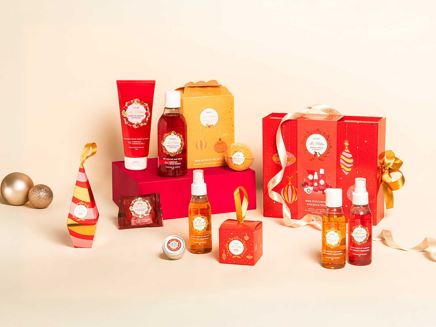 Découvrez un assortiment de produits de beauté parfumés à la pomme d'amour, présentés dans des emballages festifs rouges et dorés, parfaits pour un cadeau enchanteur.