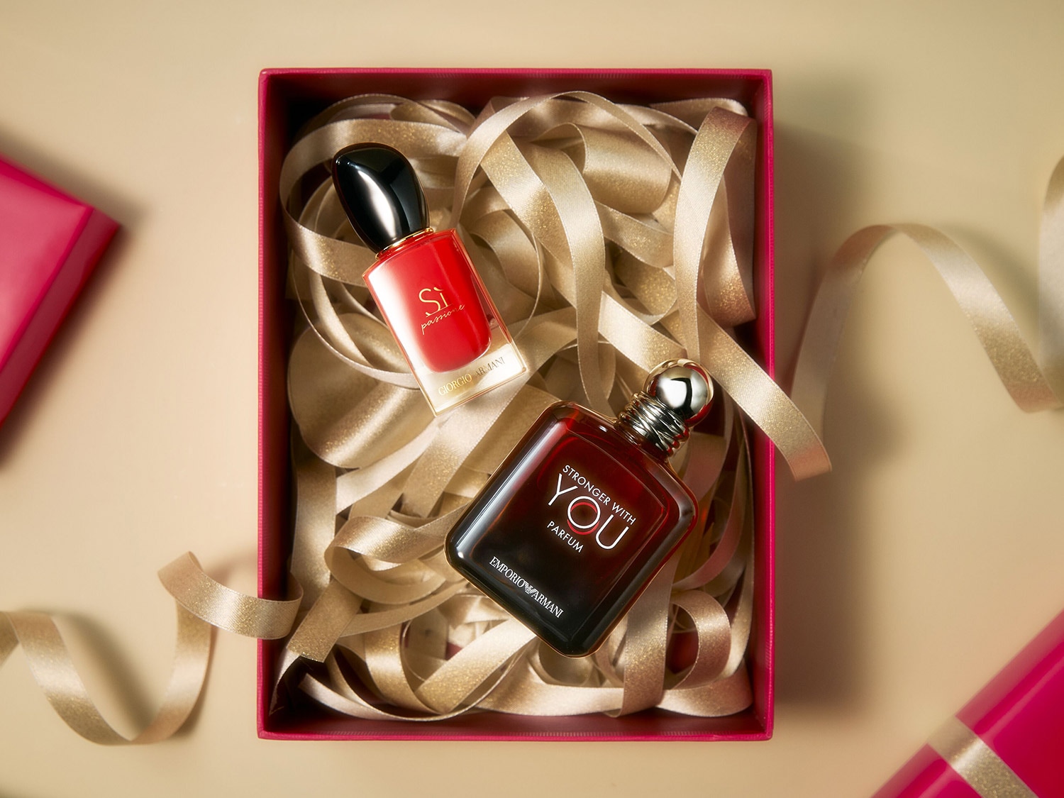 Dans une boîte rose, deux parfums Emporio Armani, Si Passione rouge et Stronger With You ambré, reposent sur des rubans dorés, offrant un duo olfactif captivant.