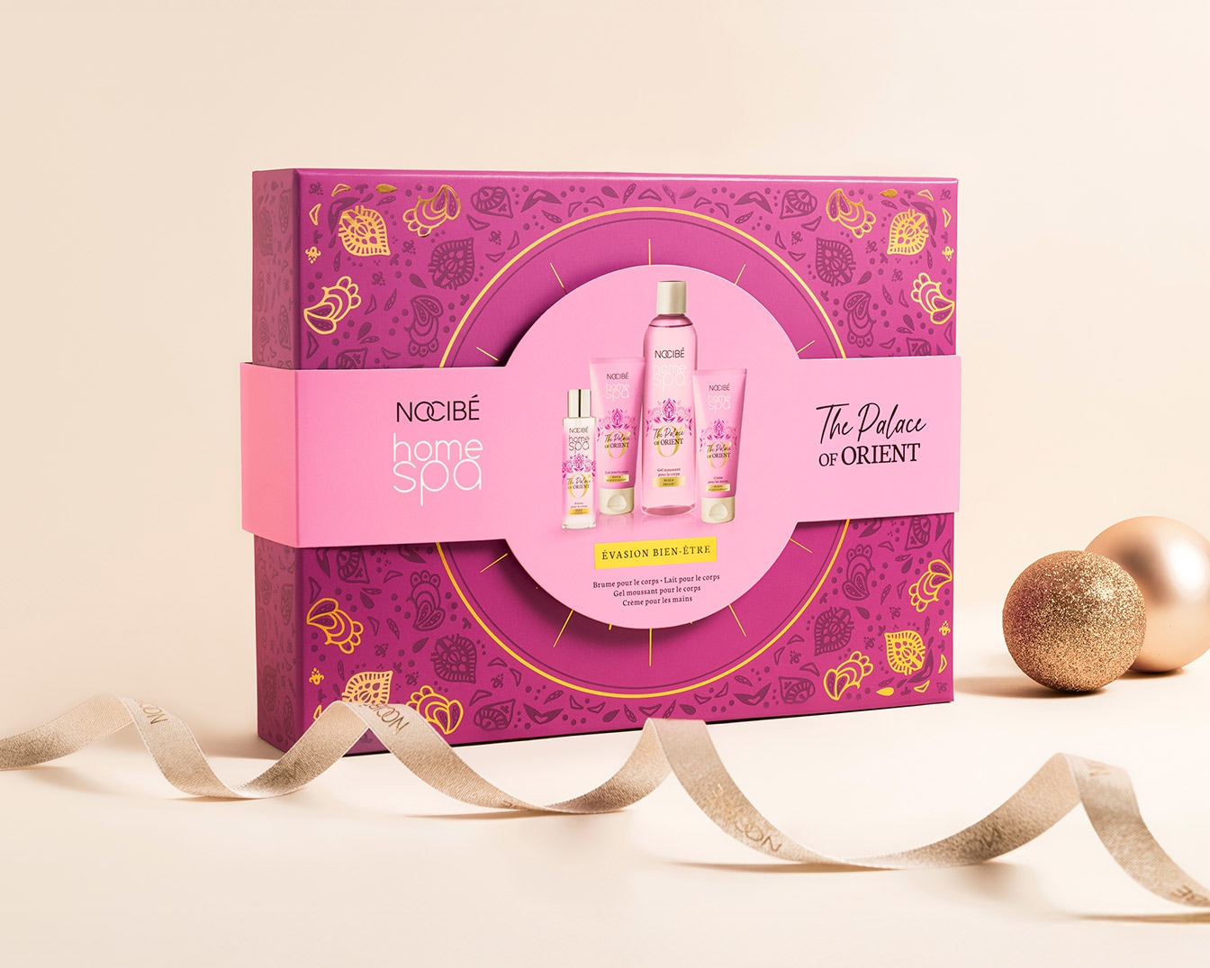 Découvrez le coffret Nocibé Home Spa The Palace of Orient, un écrin violet et or contenant des produits de soin pour le corps, présentés avec un ruban doré et des boules décoratives.