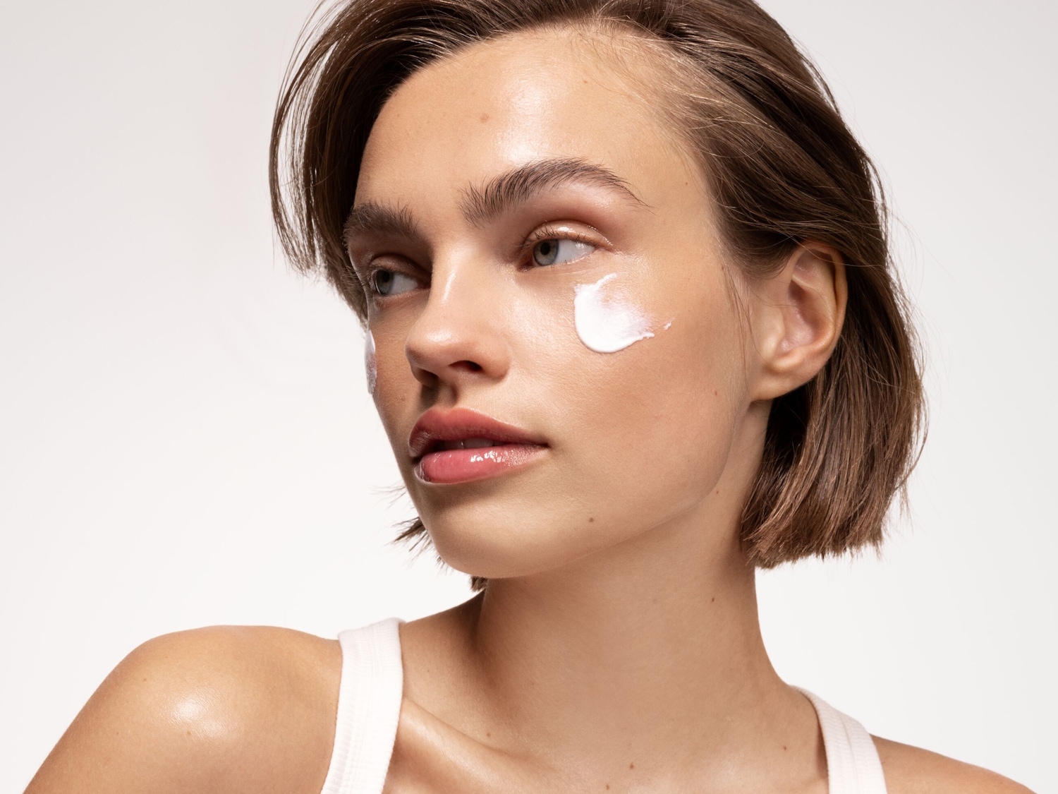 Nahaufnahme eines Models mit einem Klecks weißer Creme auf der Wange, das für Hautpflege wirbt.