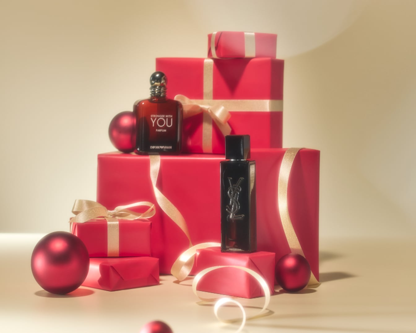 Découvrez les parfums Emporio Armani et Yves Saint Laurent, présentés sur des cadeaux rouges et des décorations festives dorées, parfaits pour les fêtes.