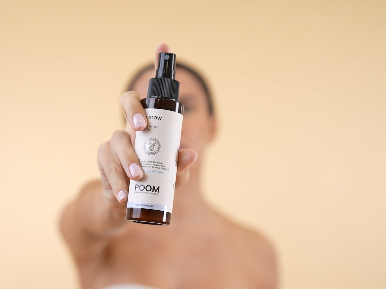 Aquí se muestra un frasco de spray blanco y marrón de POOM Korean Scientific Cosmetics, sostenido por una mano, con la etiqueta GLOW ATU PIEL DIA.