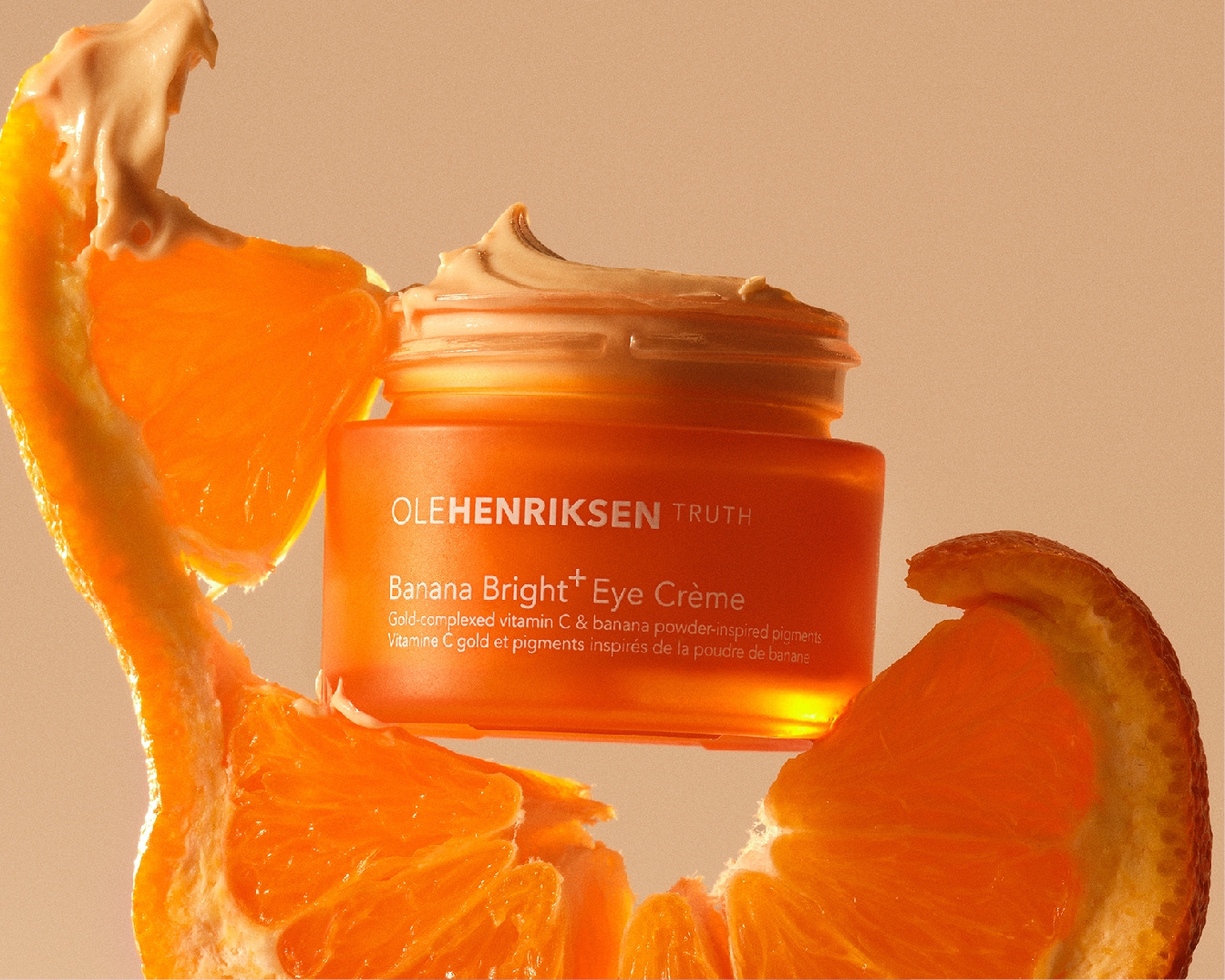 Oranje potje Ole Henriksen Truth Banana Bright+ Eye Crème, verrijkt met vitamine C en bananenpoederpigmenten, omringd door verse sinaasappelschijfjes.