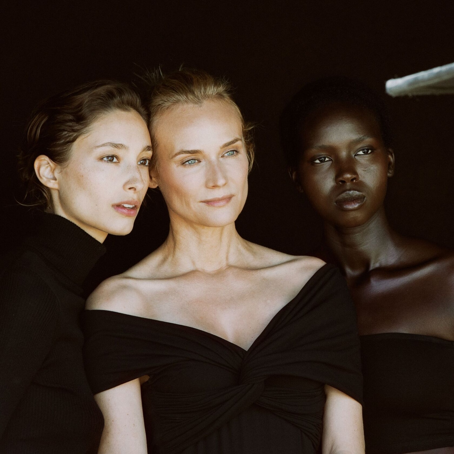 Trois femmes aux teints variés posent ensemble, vêtues de noir, créant un contraste saisissant et élégant.