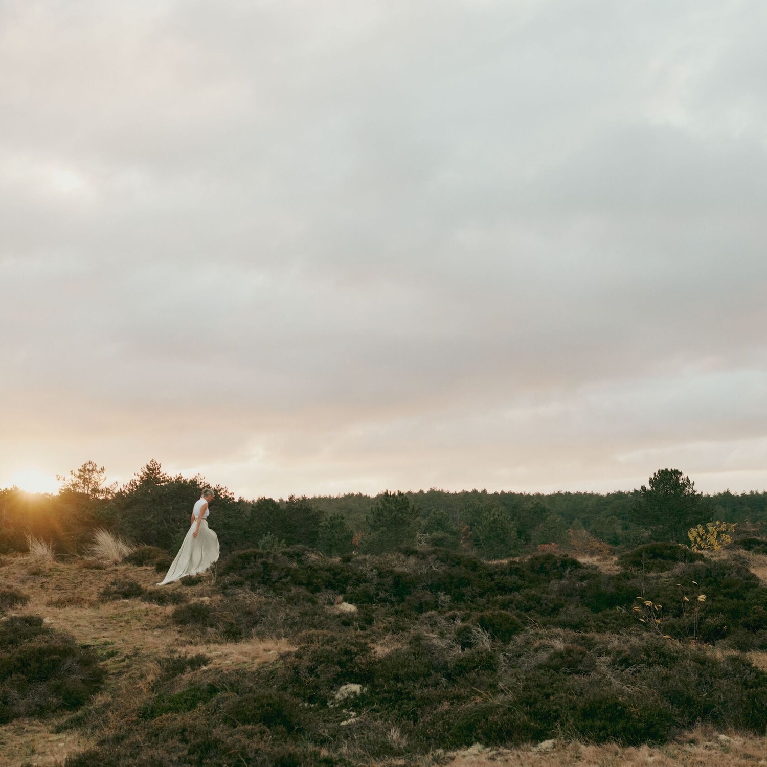 Une femme en robe fluide marche dans un paysage naturel au coucher du soleil, évoquant la liberté et la sérénité.