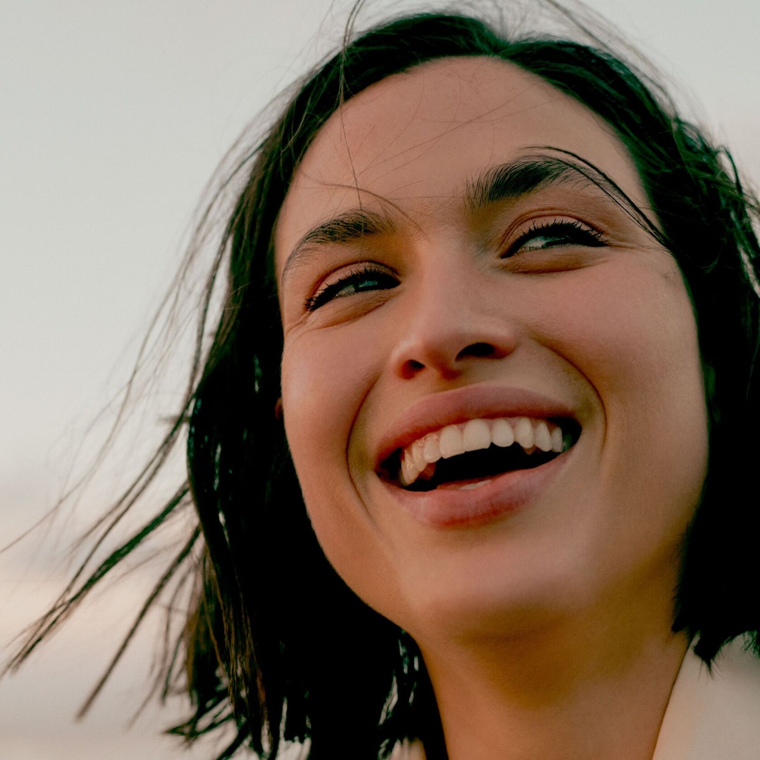 Portrait d'une jeune femme souriante aux cheveux noirs, regardant vers le haut avec une expression joyeuse.