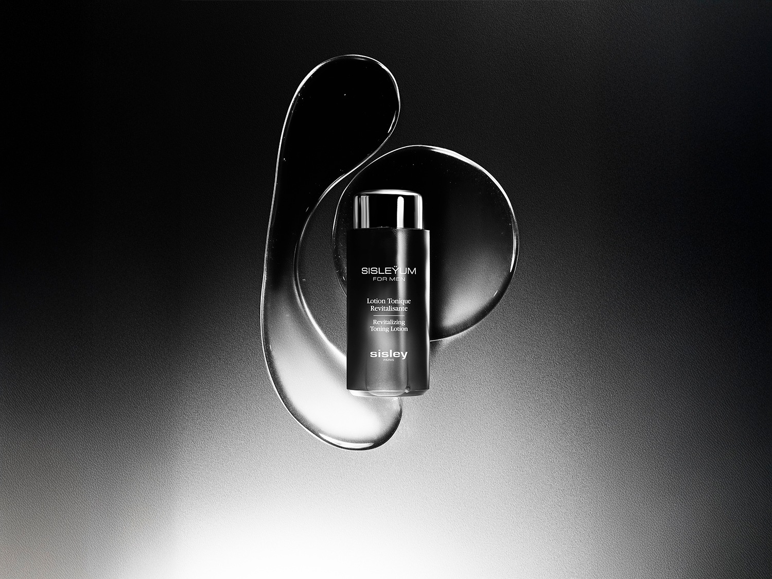 Czarna butelka toniku Sisleyum For Men Revitalizing Toning Lotion otoczona przezroczystymi elementami na ciemnym tle.