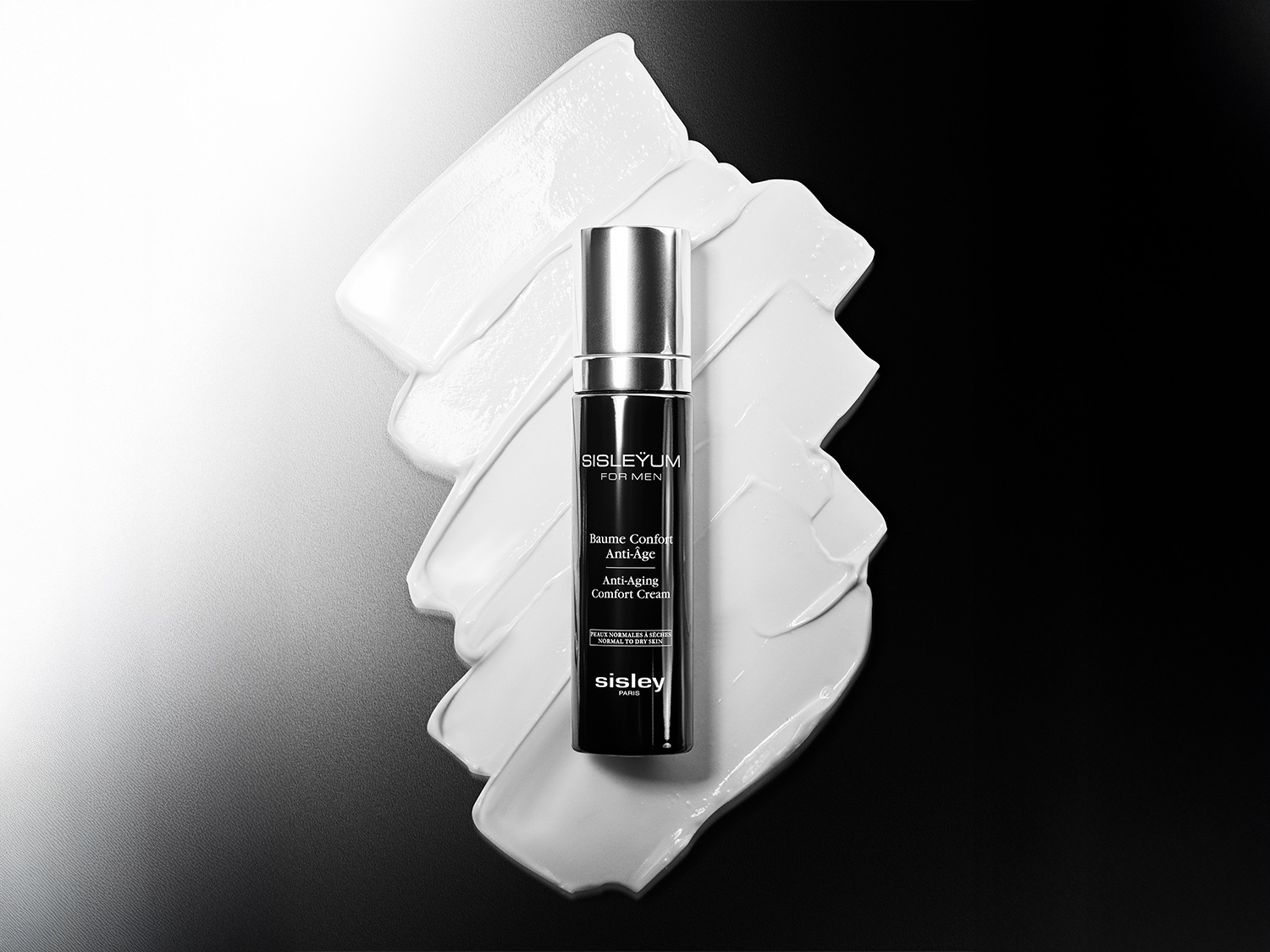 Czarna butelka balsamu Sisleyum For Men Anti-Âge otoczona białymi smugami kremu, oferująca komfort i działanie przeciwstarzeniowe dla skóry normalnej i suchej.