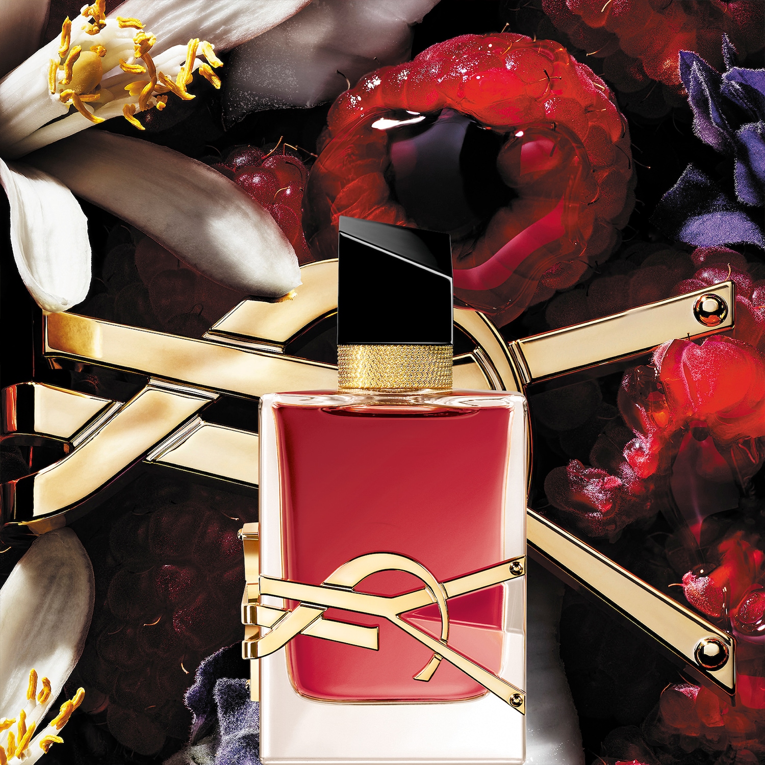 Een rechthoekige parfumfles met rode vloeistof en een gouden YSL-logo staat tegen een achtergrond van bloemen en frambozen.
