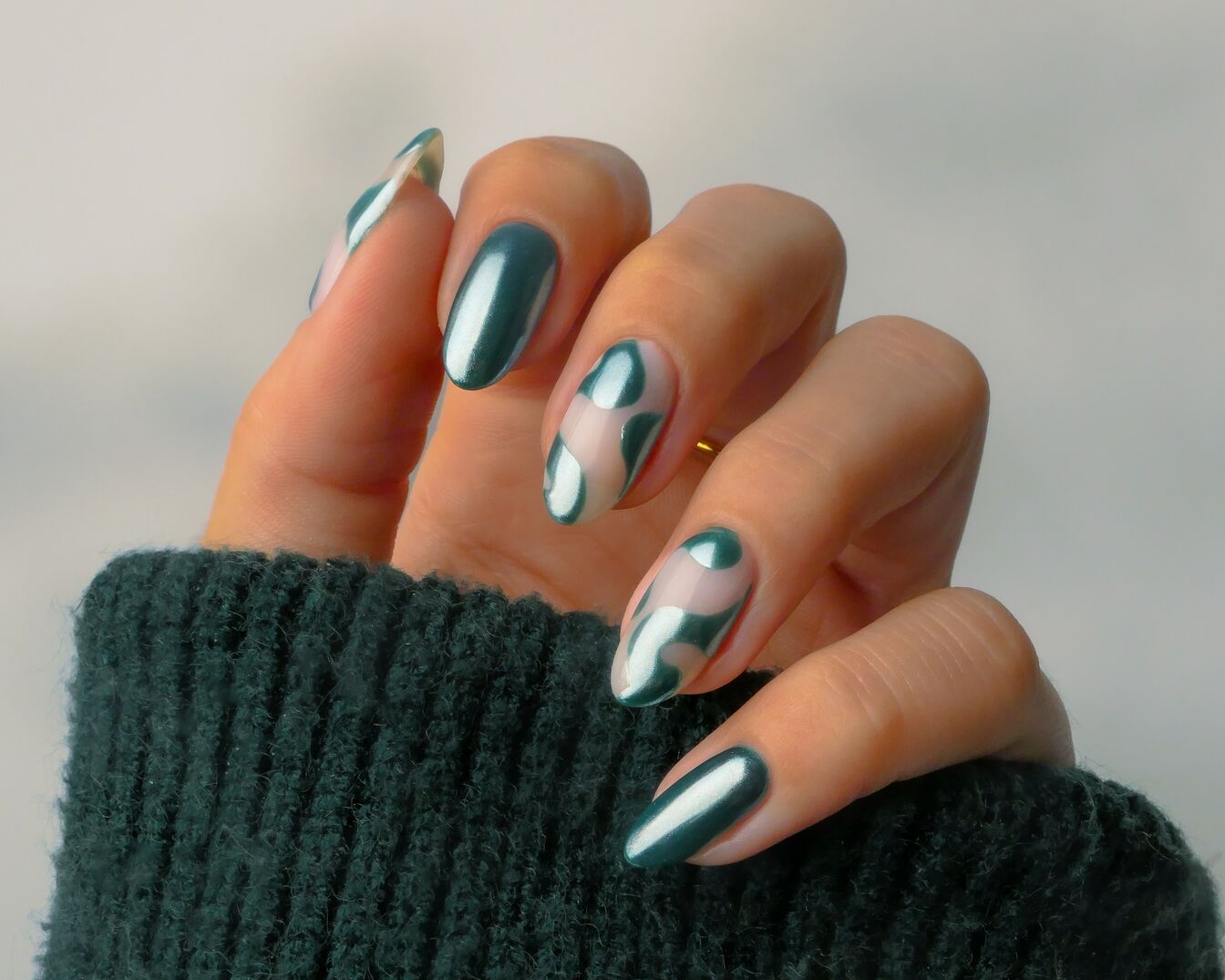 Nahaufnahme einer Hand mit smaragdgrünen Nägeln, einige davon mit abstrakten, unregelmässigen Formen, die einen modernen und künstlerischen Look erzeugen.