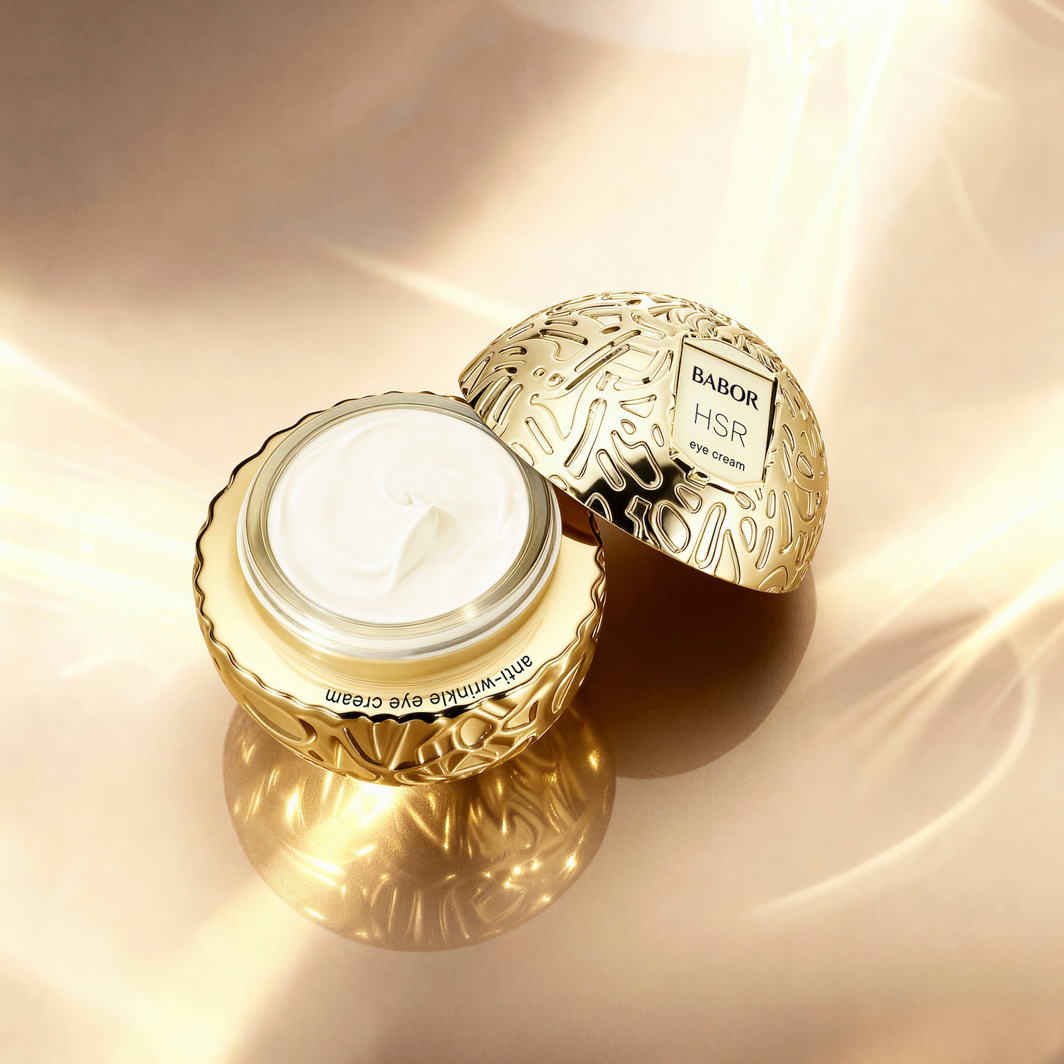 Nahaufnahme einer goldenen Dose Babor HSR Anti-Falten-Augencreme mit geöffnetem Deckel, die eine weiße Creme zeigt, auf einem goldenen Hintergrund.