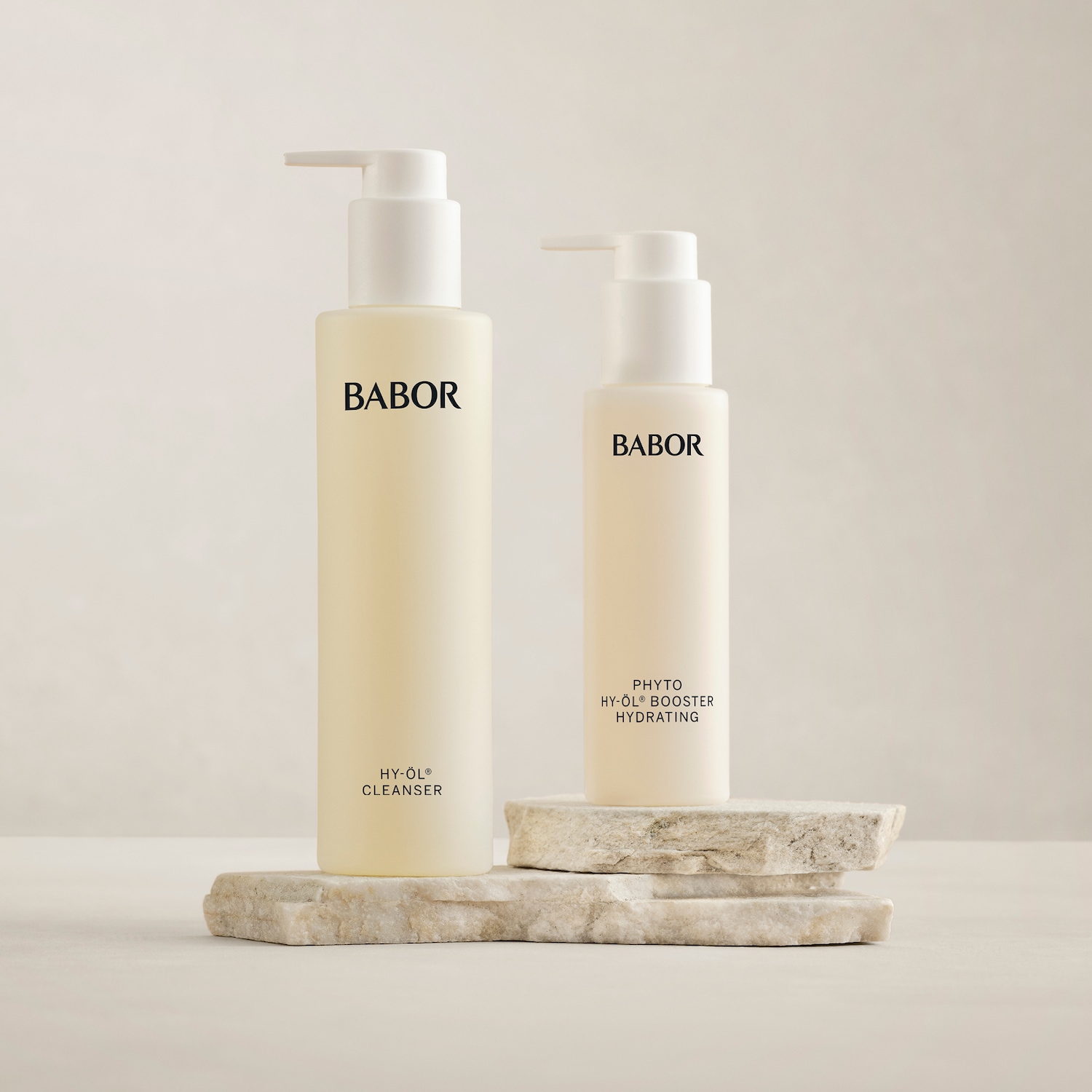 Zwei Babor-Produkte stehen auf einem Stein: HY-ÖL Reiniger in einer hellgelben Flasche und PHYTO HY-ÖL Booster Hydrating in einer kleineren Flasche.