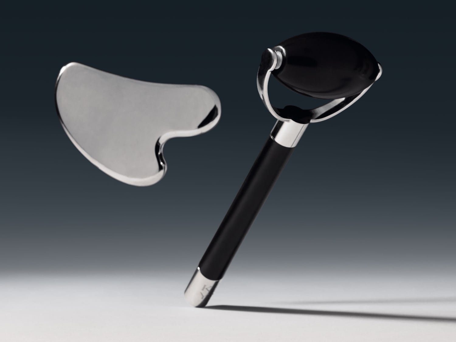 Černý obličejový váleček s rukojetí a stříbrný kámen Gua Sha pro masáž obličeje.