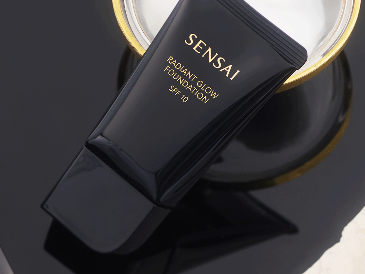 Czarna tuba Sensai Radiant Glow Foundation SPF 10 zapewnia promienny wygląd i ochronę przed słońcem.