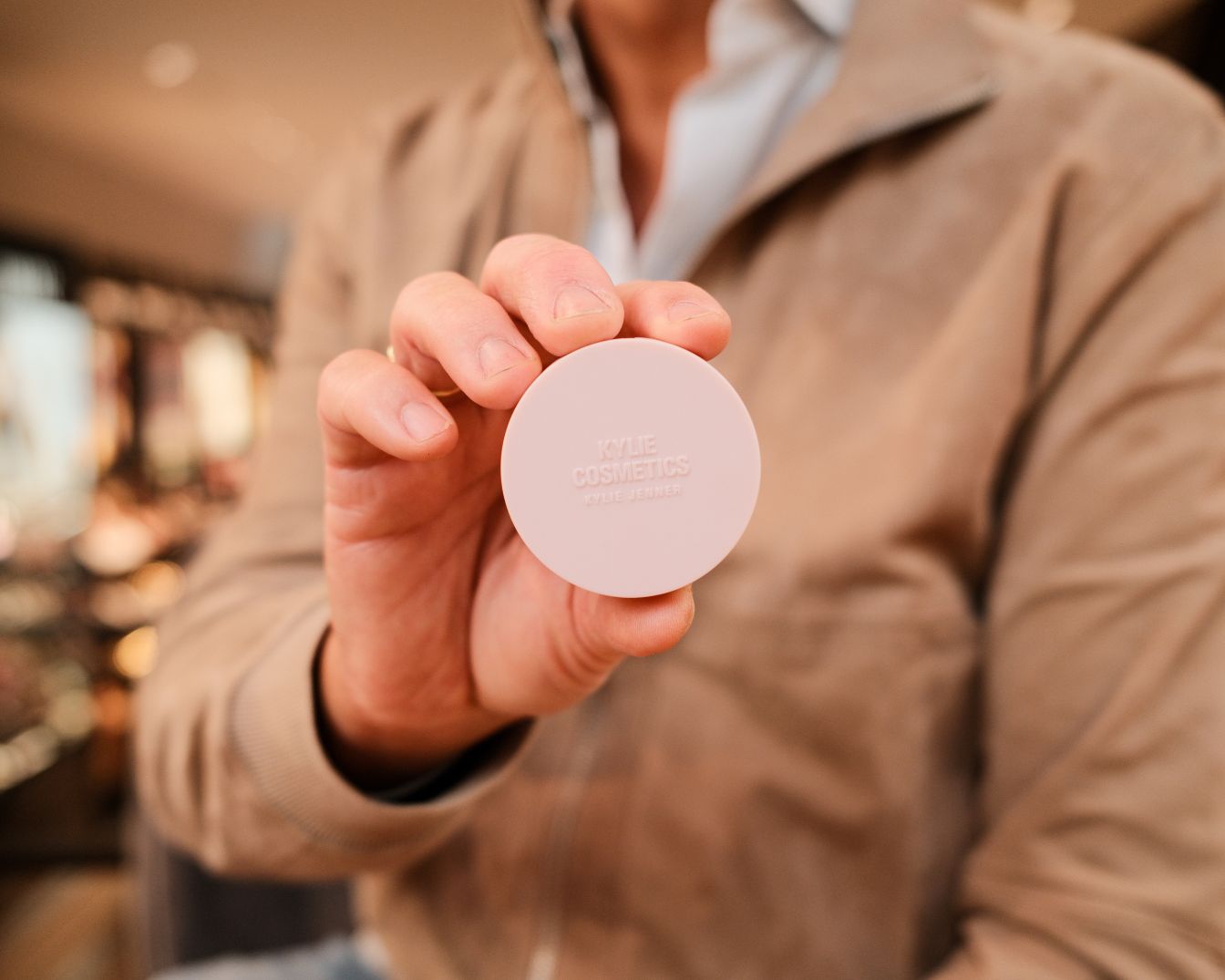 Een persoon houdt een lichtroze, ronde Kylie Cosmetics poederdoos vast, perfect voor een touch-up onderweg.