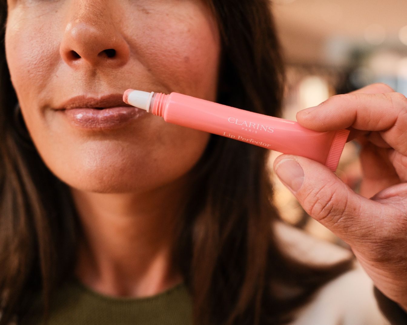 Een vrouw brengt Clarins Lip Perfector aan, een roze lipgloss, voor een subtiele glans.