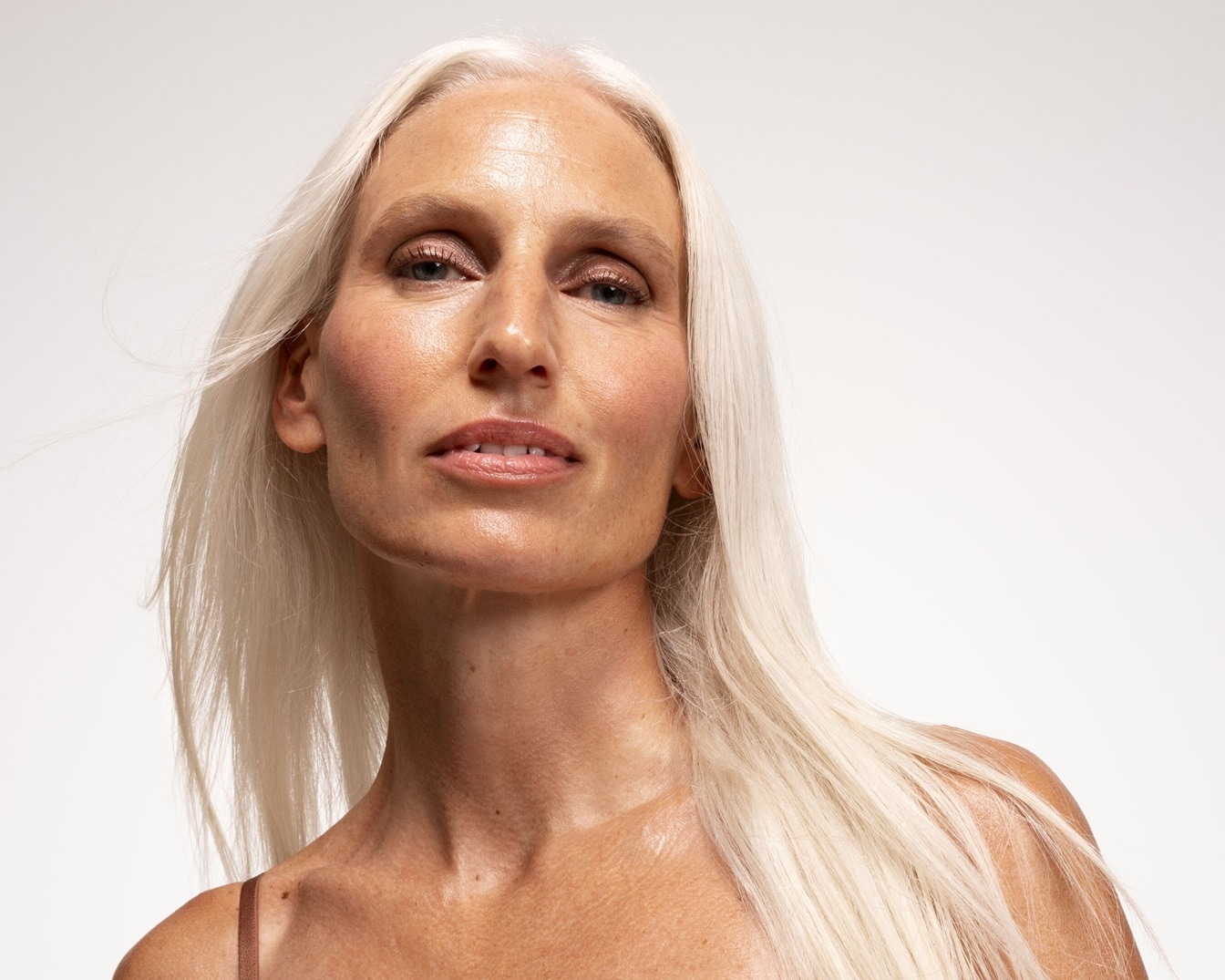 Porträt einer Frau mit langen, glatten, weißen Haaren, die ein natürliches Make-up mit rosa Rouge und glänzenden Lippen trägt.