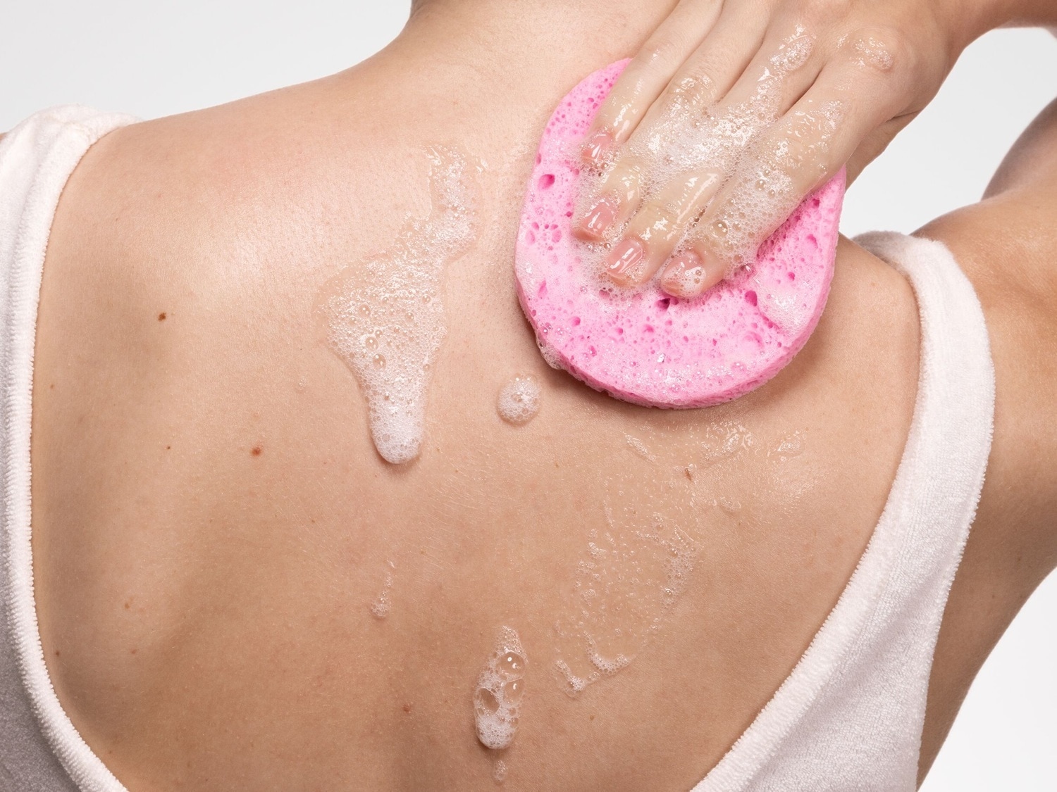 Eine Person verwendet einen rosa Badeschwamm mit Seife, um den Rücken zu reinigen.