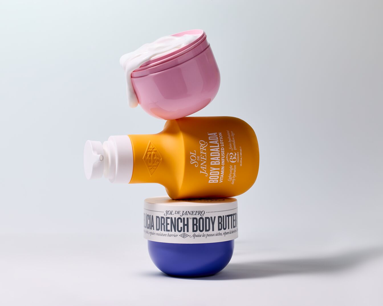 Aufeinander gestapelte Sol de Janeiro Körperpflegeprodukte: ein rosa Tiegel mit weißer Creme, eine gelbe Lotion und eine blaue Körperbutter.