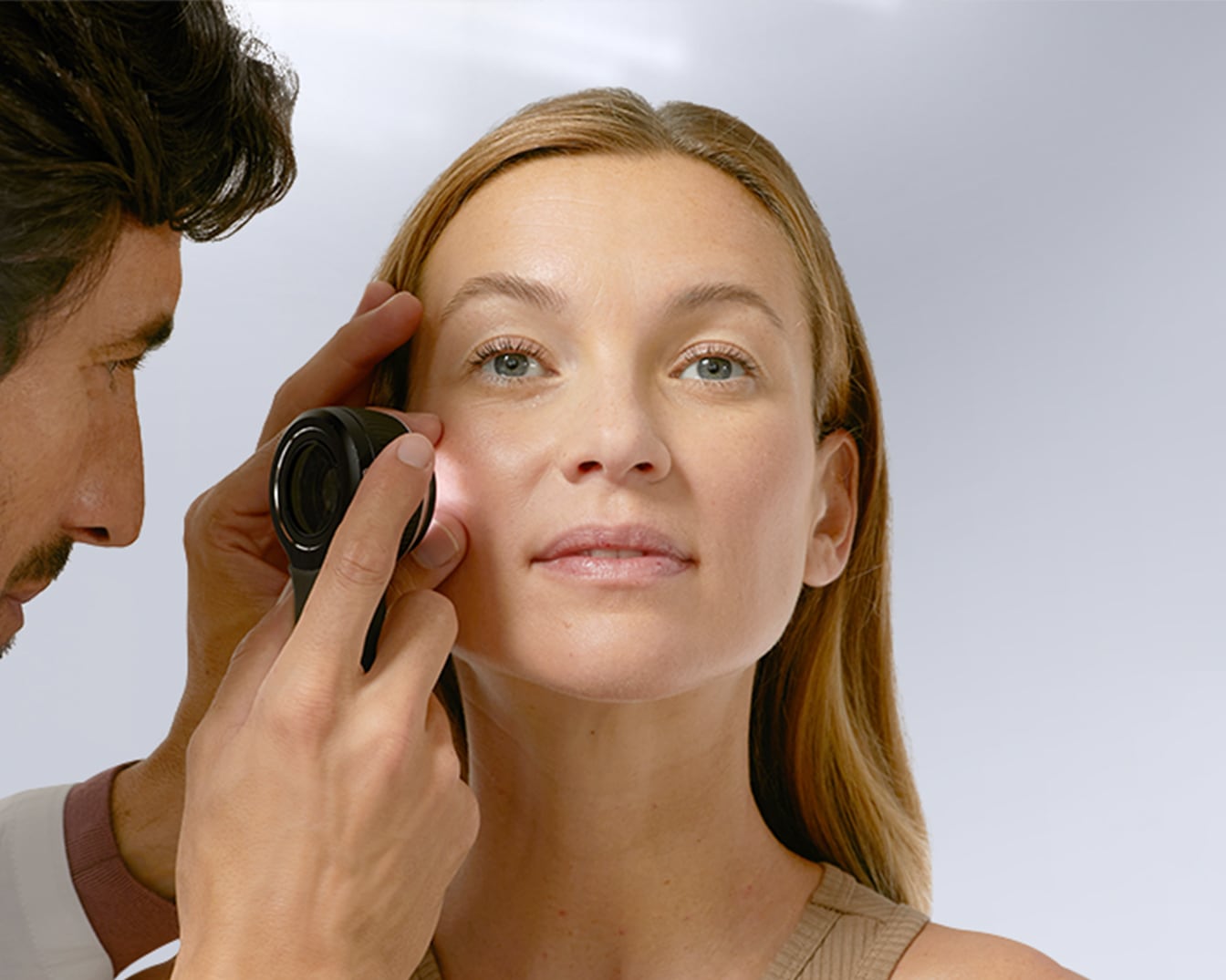 Un dermatologo esamina la pelle chiara di una donna con una lente d'ingrandimento illuminata per valutare la salute e le condizioni della sua pelle.