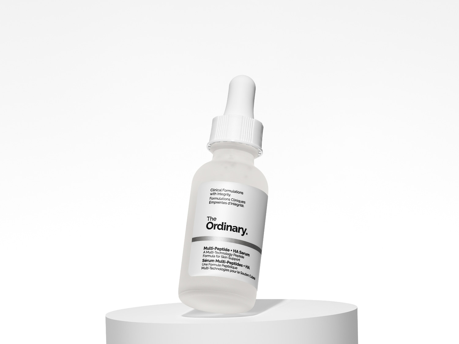 Das Ordinary Multi-Peptide + HA Serum in einer durchsichtigen Glasflasche mit Pipette, die auf einer weißen Oberfläche steht.