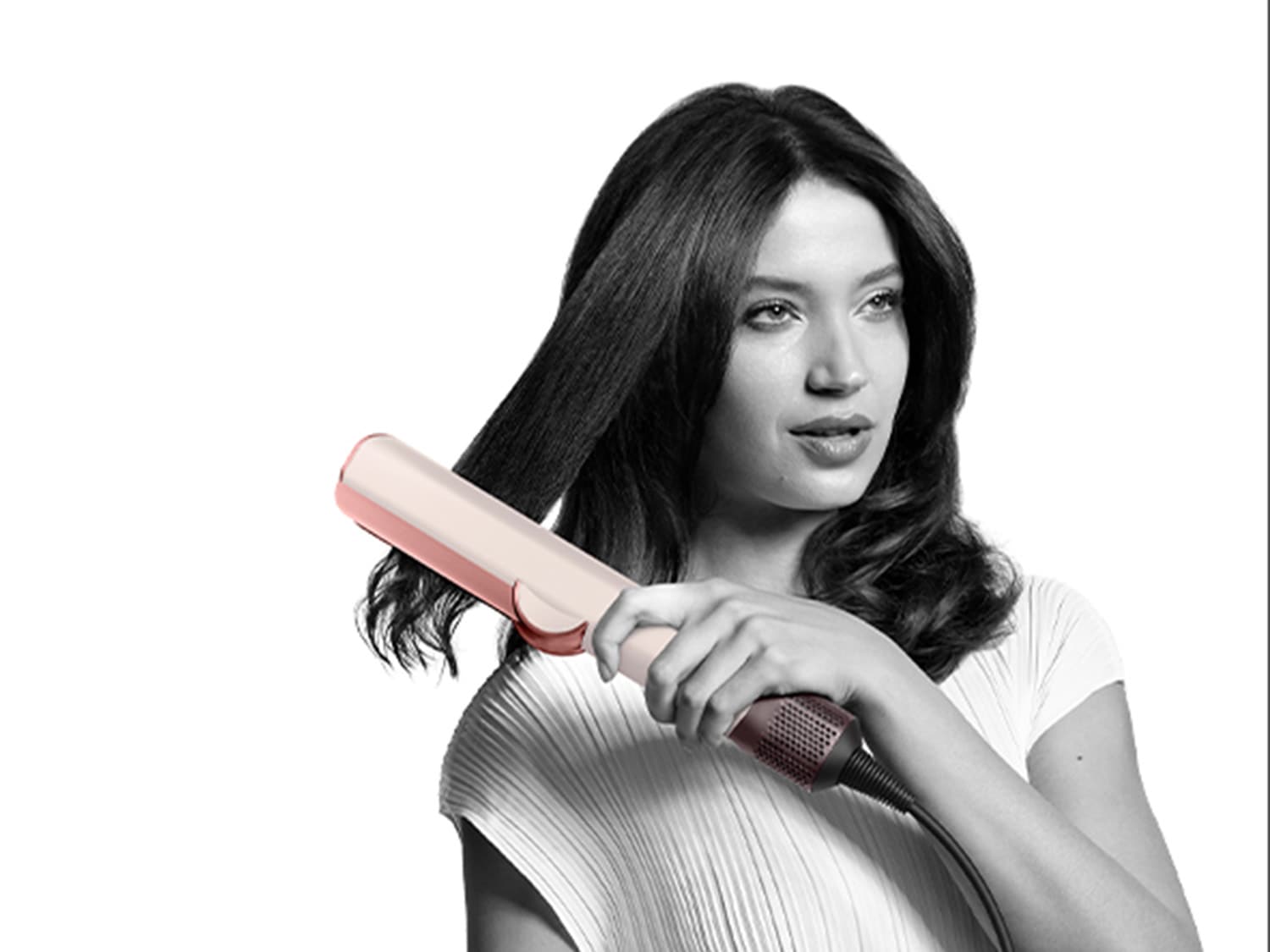 Eine Frau mit dunklen, gewellten Haaren glättet eine Strähne mit einem rosafarbenen Glätteisen, um einen eleganten Look zu erzielen.