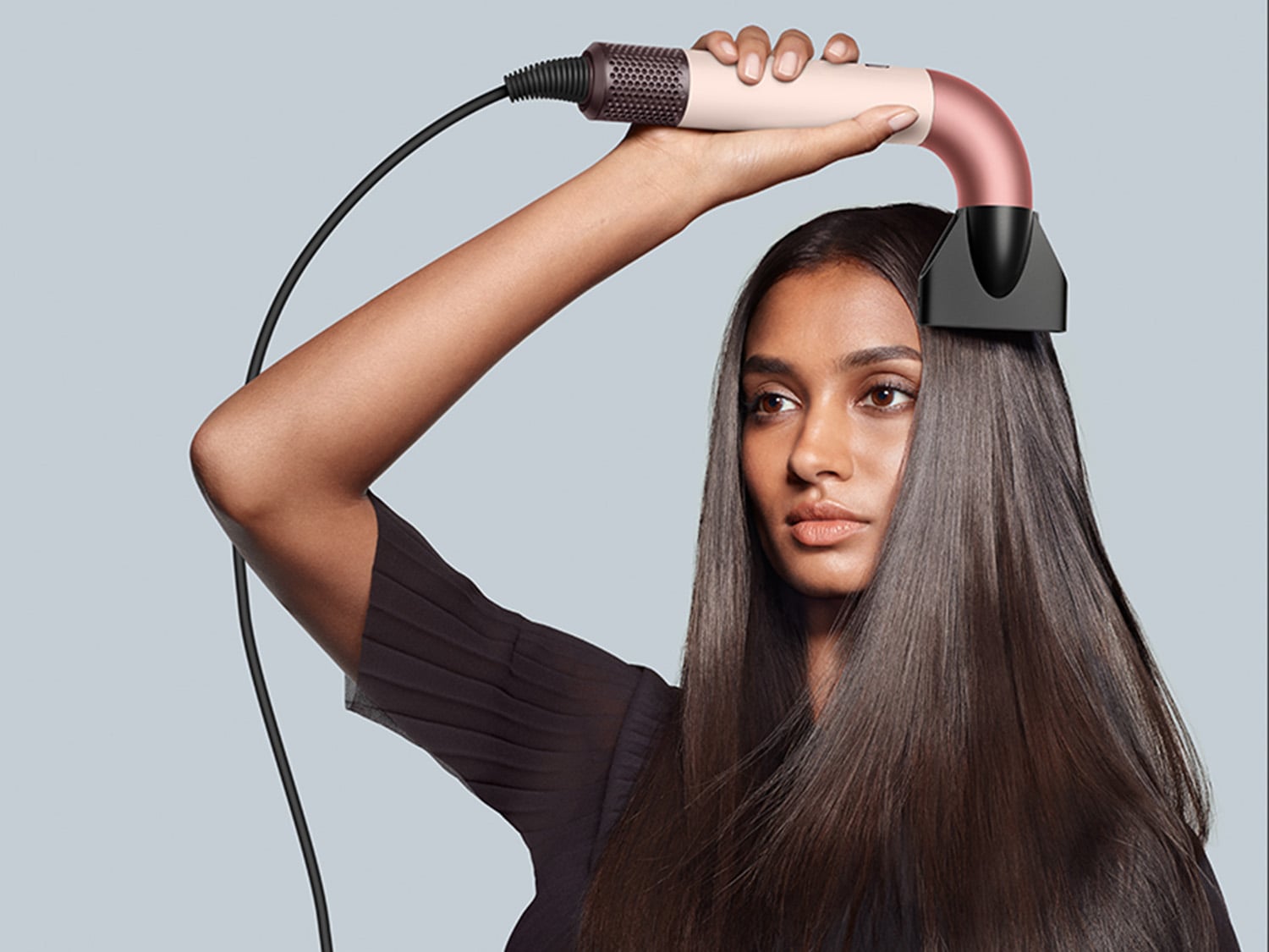 Eine Frau mit langen, glatten, braunen Haaren benutzt eine Stylingbürste mit einem hellrosa Griff und einem schwarzen Bürstenkopf, um ihr Haar zu stylen.