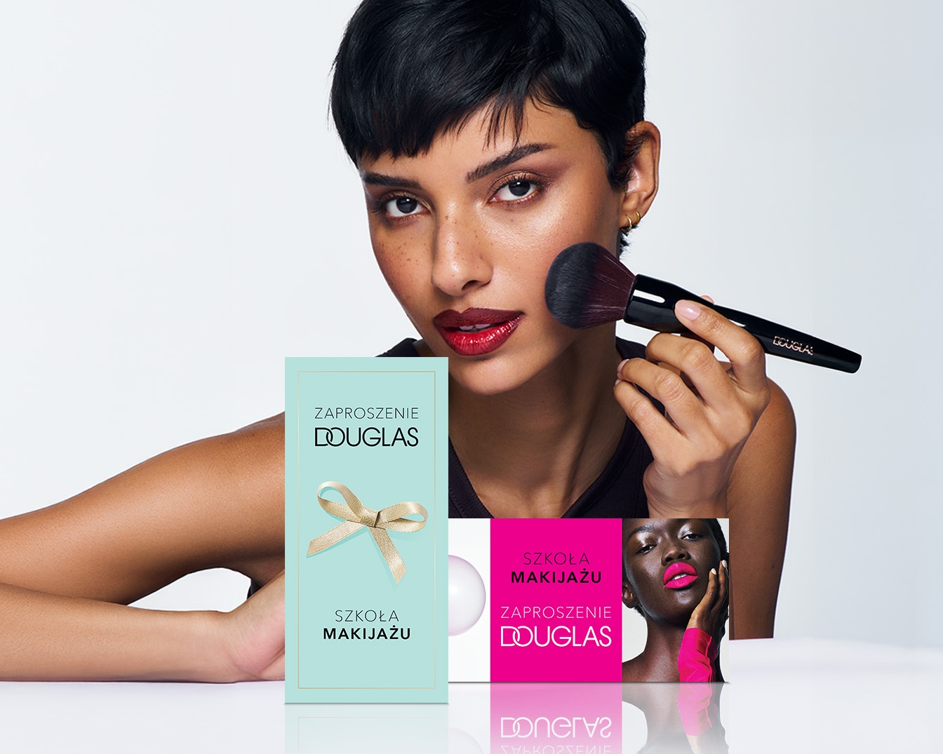 Kobieta z krótkimi włosami nakłada makijaż pędzlem Douglas, obok zaproszenie na Szkołę Makijażu Douglas.