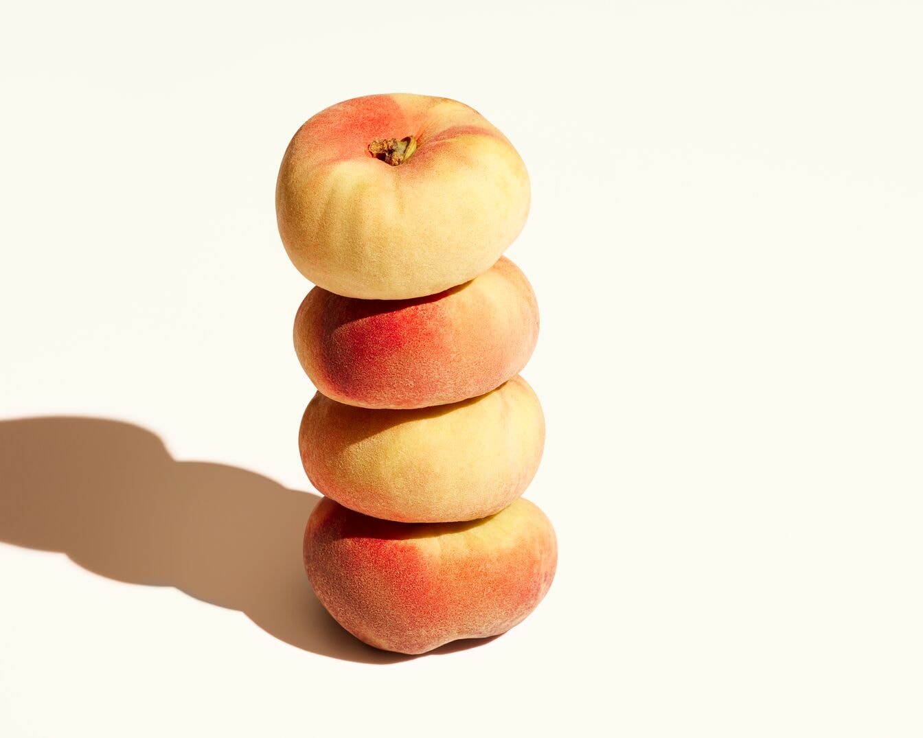 Ein Stapel von vier flachen Pfirsichen, die sich durch ihre gelb-rote Farbe und ihre einzigartige Form auszeichnen.