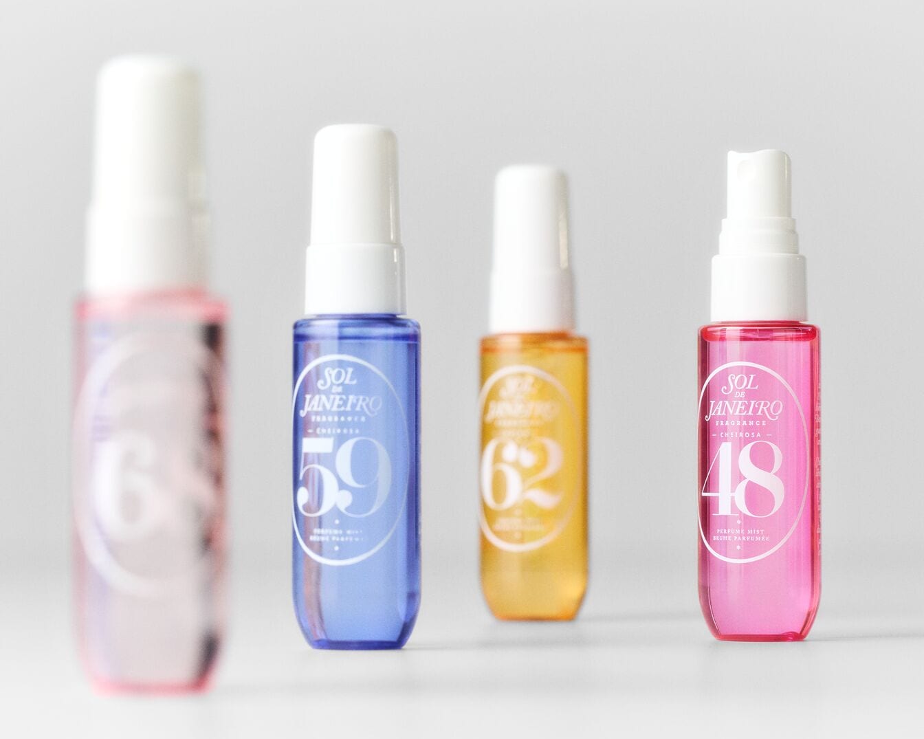 Vier Sol de Janeiro Duftsprays in Rosa, Blau, Gelb und Pink mit weißen Kappen, die die Nummern 6, 59, 62 und 48 tragen.