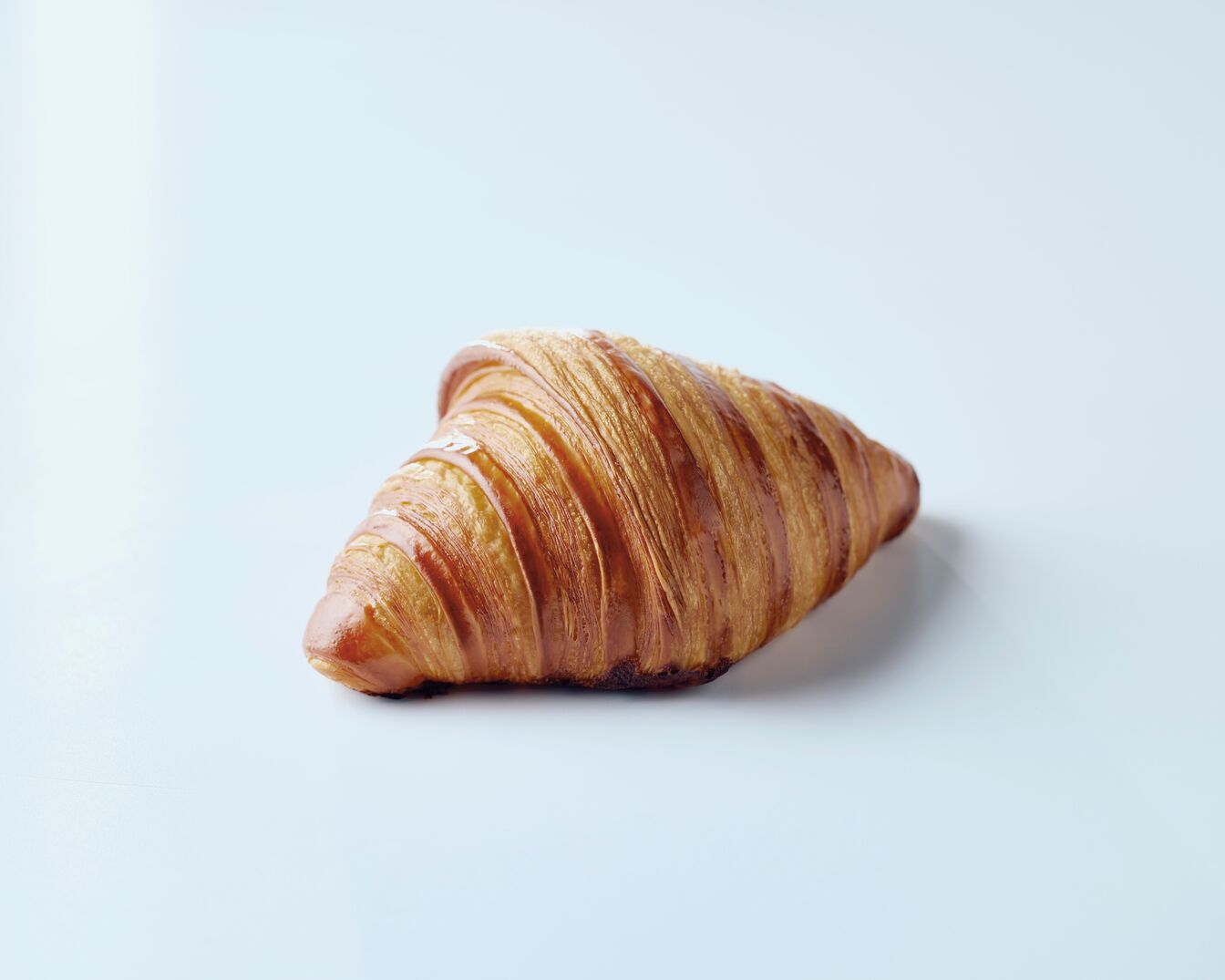 Ein goldbraunes Croissant mit knuspriger Kruste liegt auf einem hellen Untergrund und lädt zum Genießen ein.