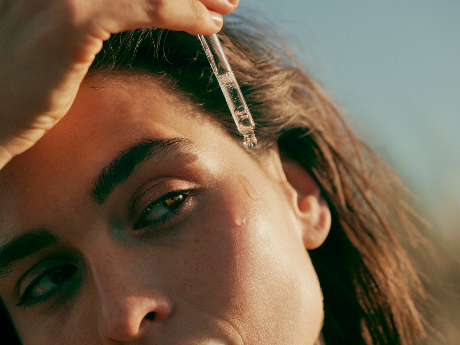 Gros plan sur une femme appliquant un sérum transparent avec une pipette sur sa joue, mettant en valeur l'éclat et l'hydratation de sa peau.