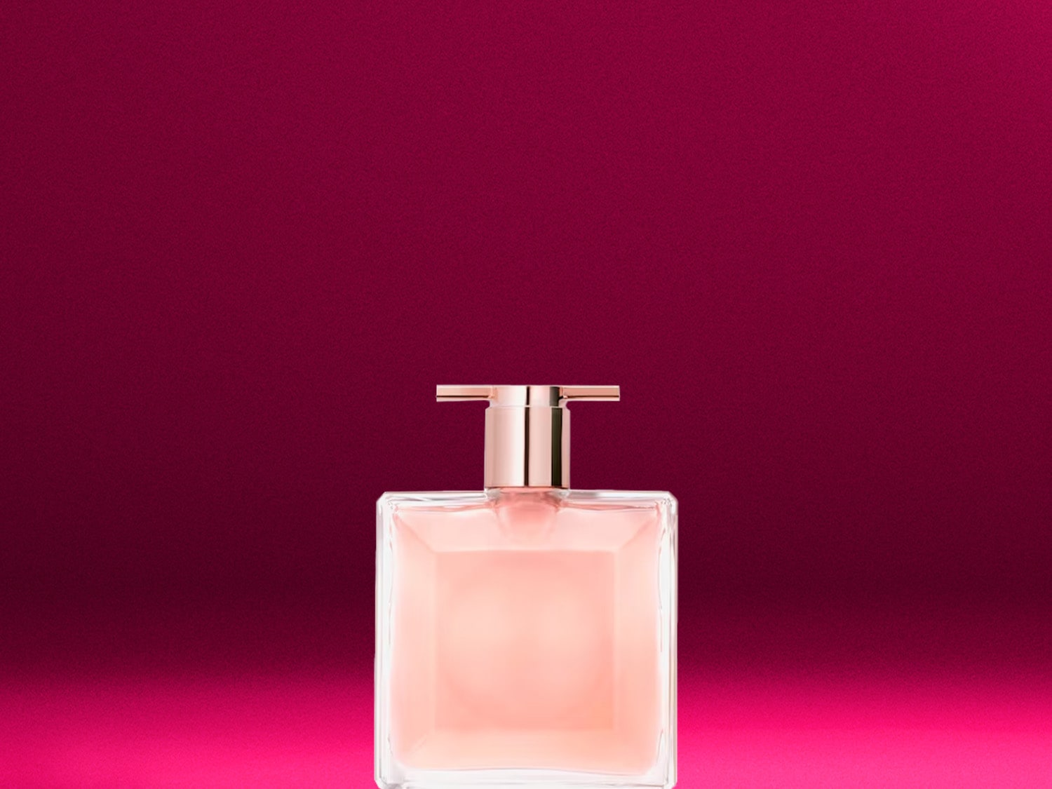 Ein rechteckiger Parfümflakon mit rosafarbenem Inhalt und goldenem Verschluss steht vor einem leuchtend pinkfarbenen Hintergrund.