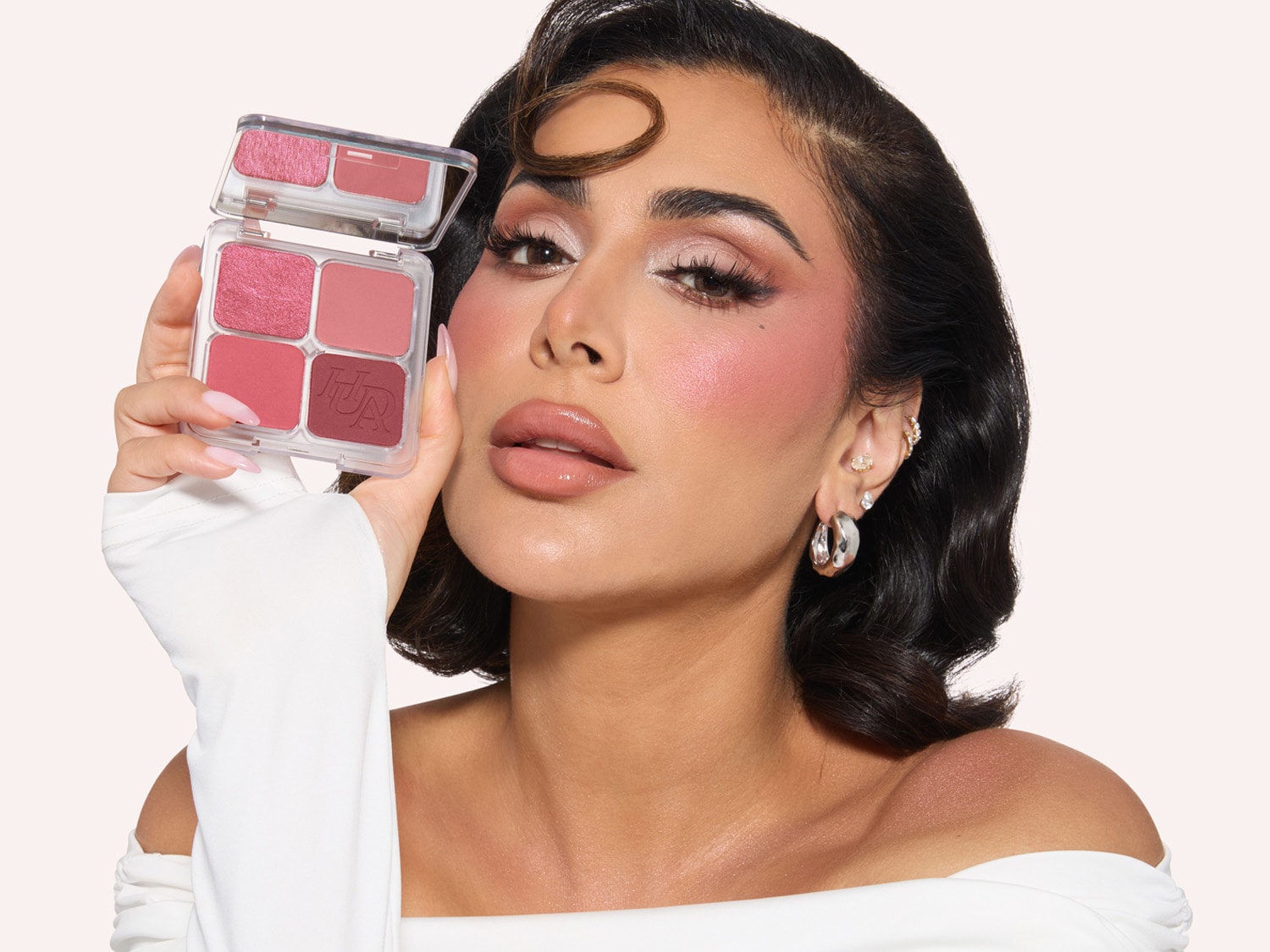 Huda Kattan hält eine transparente Palette mit vier verschiedenen Rosatönen, die von hell bis dunkel reichen.