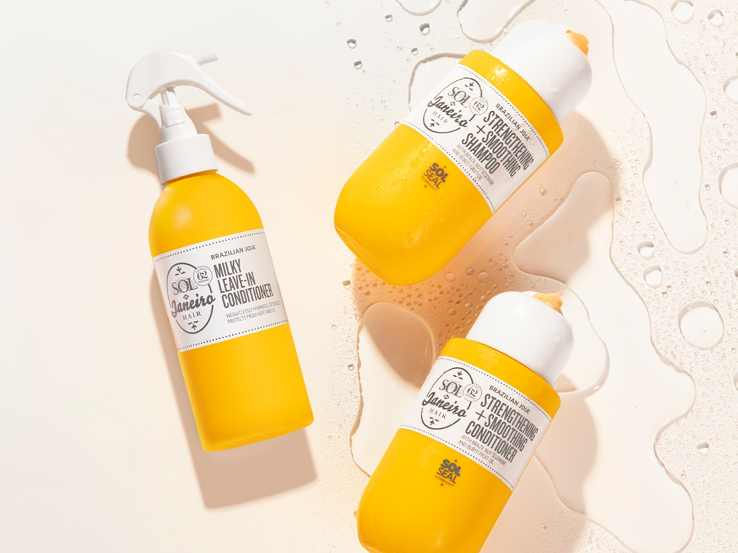 Drei gelbe Flaschen brasilianischer Joia-Haarpflegeprodukte, darunter ein Milky Leave-In Conditioner und ein Strengthening + Smoothing Shampoo und Conditioner.
