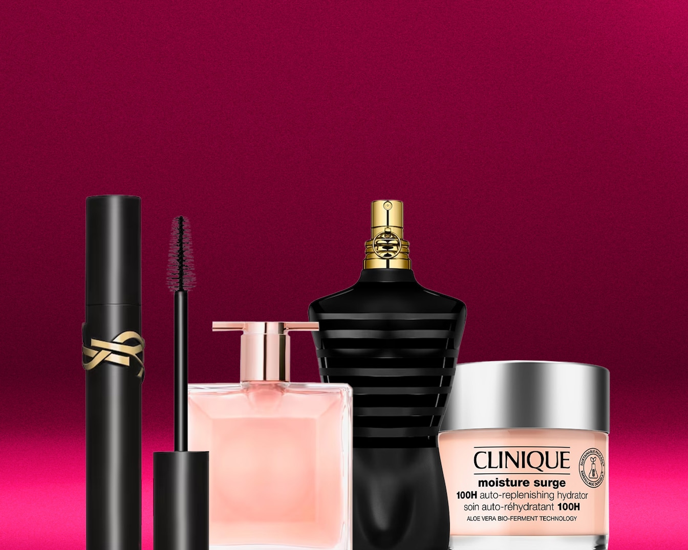 Auf einem pinkfarbenen Hintergrund sind eine schwarze YSL-Mascara, ein rosa Parfüm, ein Jean-Paul-Gaultier-Parfüm in einer schwarzen Flasche und eine Clinique Moisture Surge Creme zu sehen.