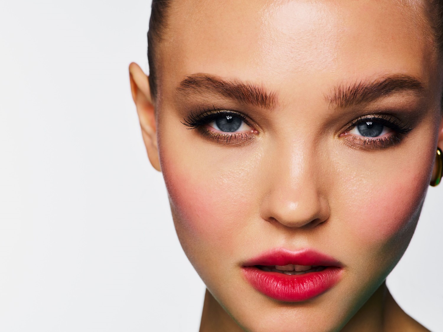 Nahaufnahme eines Frauengesichts mit strahlend blauen Augen, betont durch dunklen Lidschatten und langen Wimpern, dazu rote Lippen und rosige Wangen.