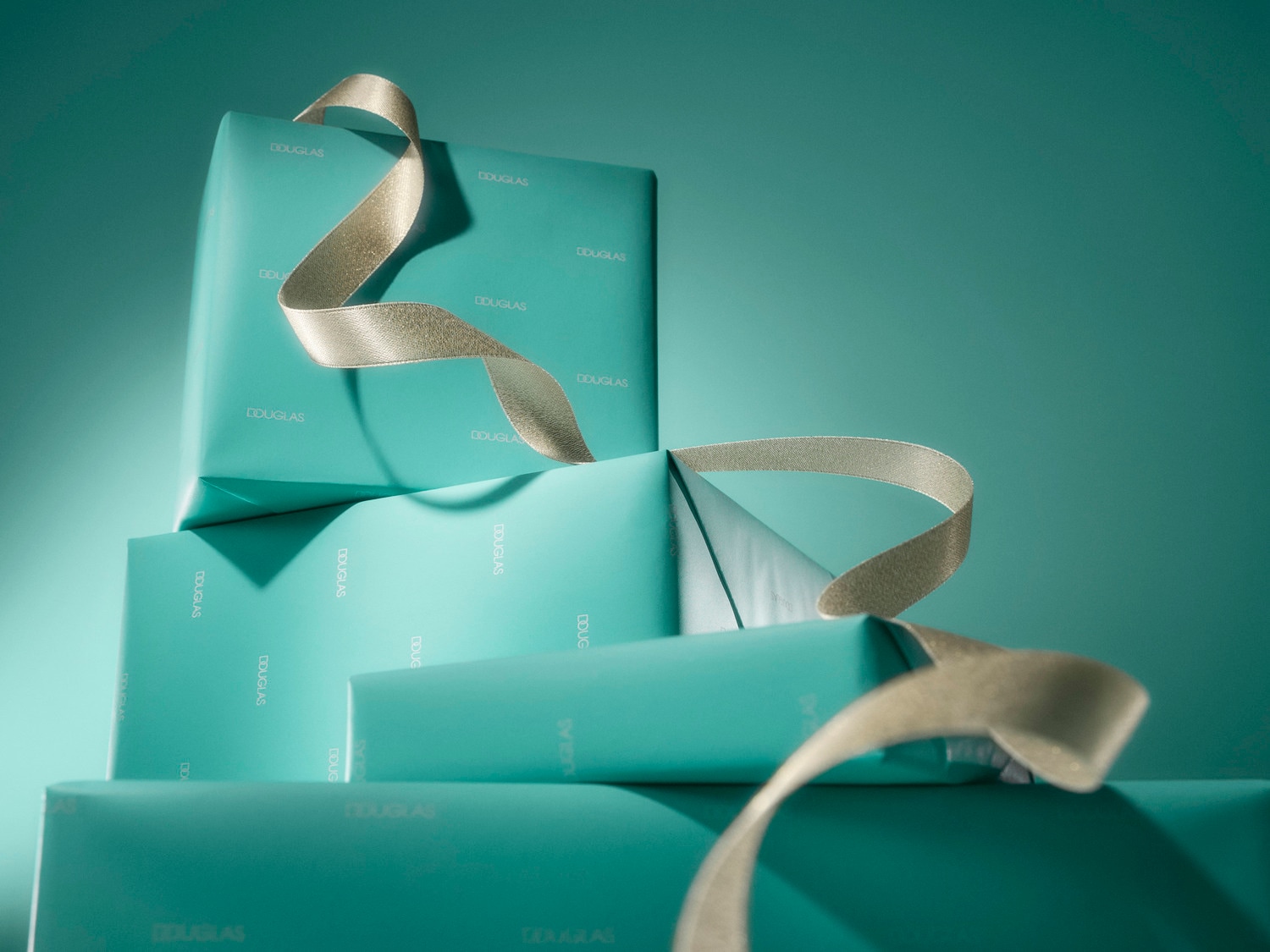 Découvrez une pile de cadeaux Douglas emballés dans du papier turquoise, ornés d'un ruban doré scintillant, parfaits pour toutes les occasions.
