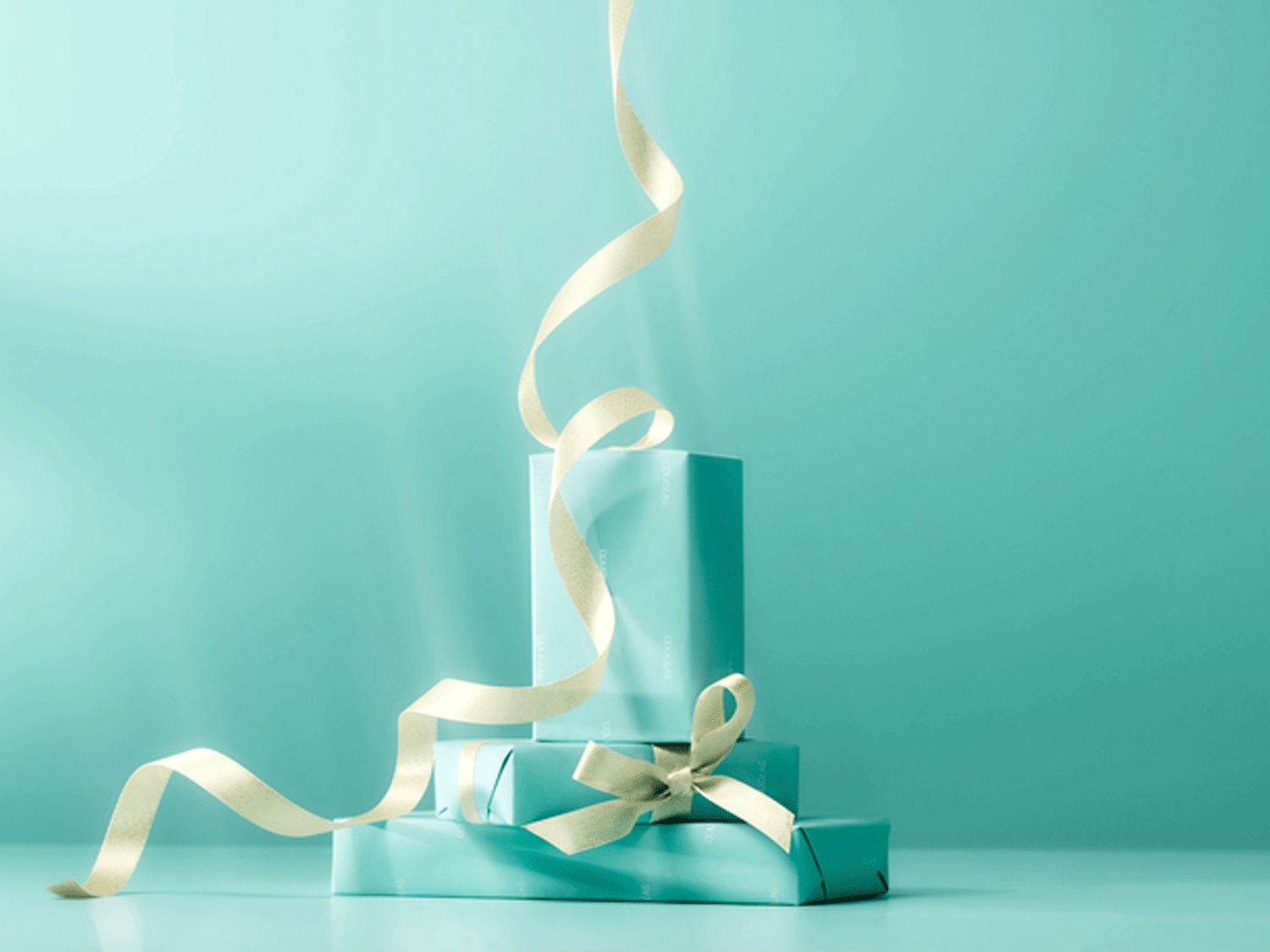 Ein Stapel helltürkiser Geschenke, gebunden mit einer cremefarbenen Schleife, vor einem passenden Hintergrund.