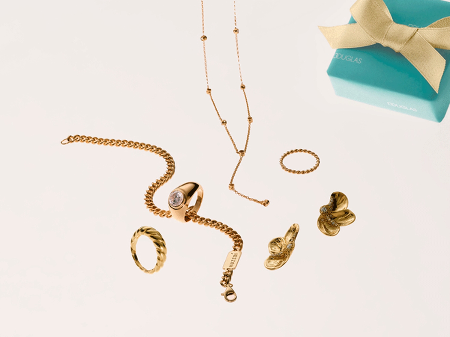 Funkelnde goldene Schmuckkollektion, darunter Halskette, Ringe, Armband und Ohrringe, zusammen mit einer hellblauen Douglas-Geschenkbox mit einer Schleife.