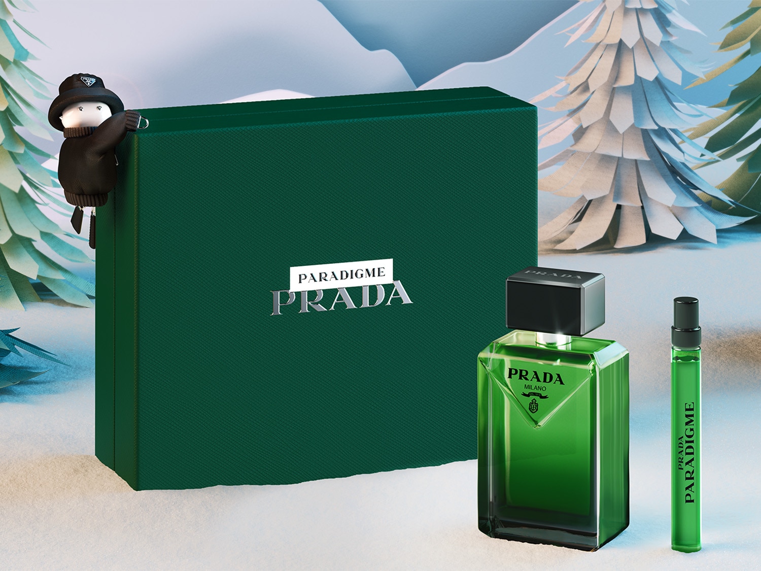Na tle zimowego krajobrazu prezentuje się zestaw Prada PARADIGME, zawierający flakon perfum, próbkę oraz eleganckie, zielone pudełko z logo marki.