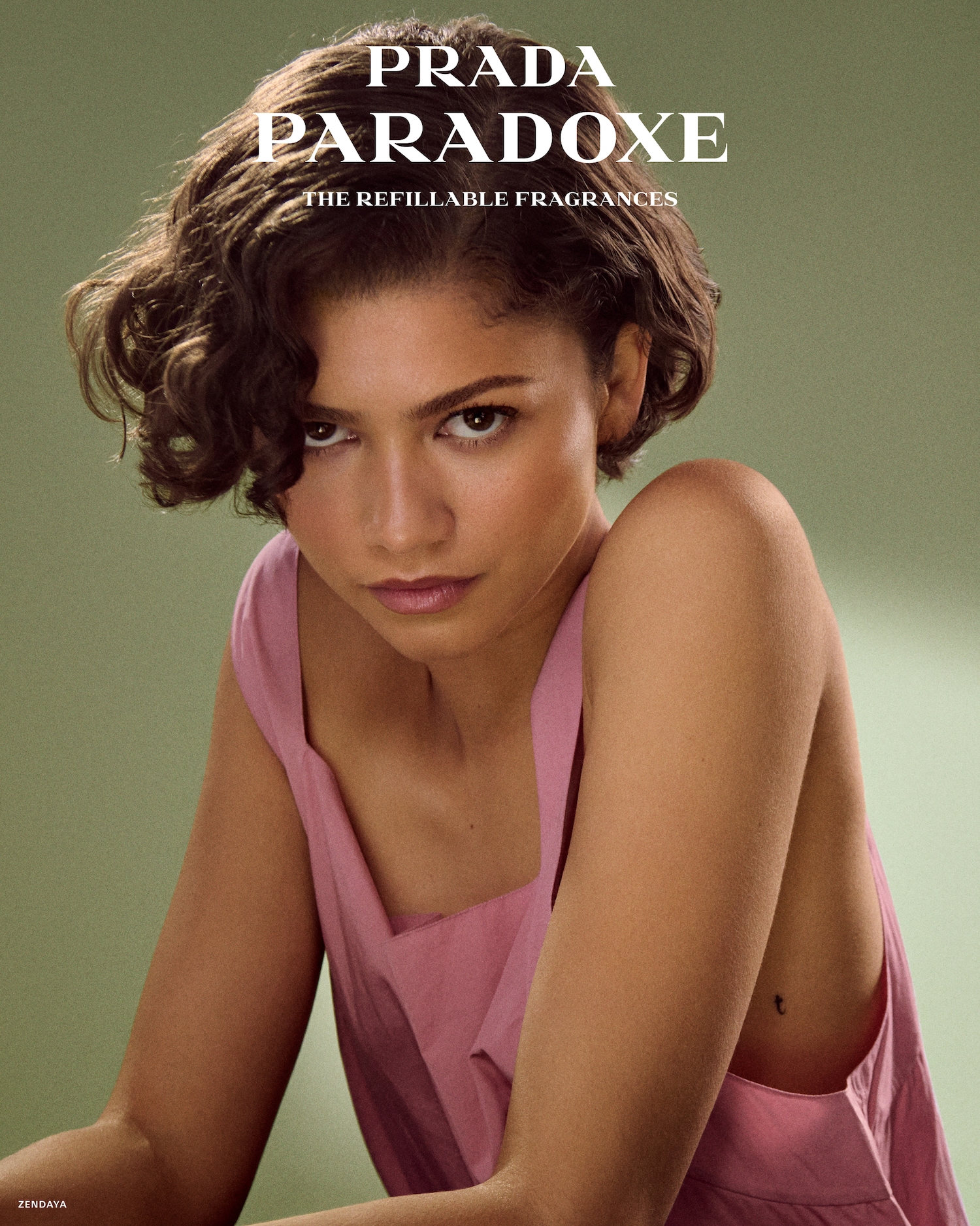 Zendaya, z krótkimi, kręconymi włosami i w różowej sukience, patrzy prosto w obiektyw, a nad nią widnieje napis "PRADA PARADOXE THE REFILLABLE FRAGRANCES".