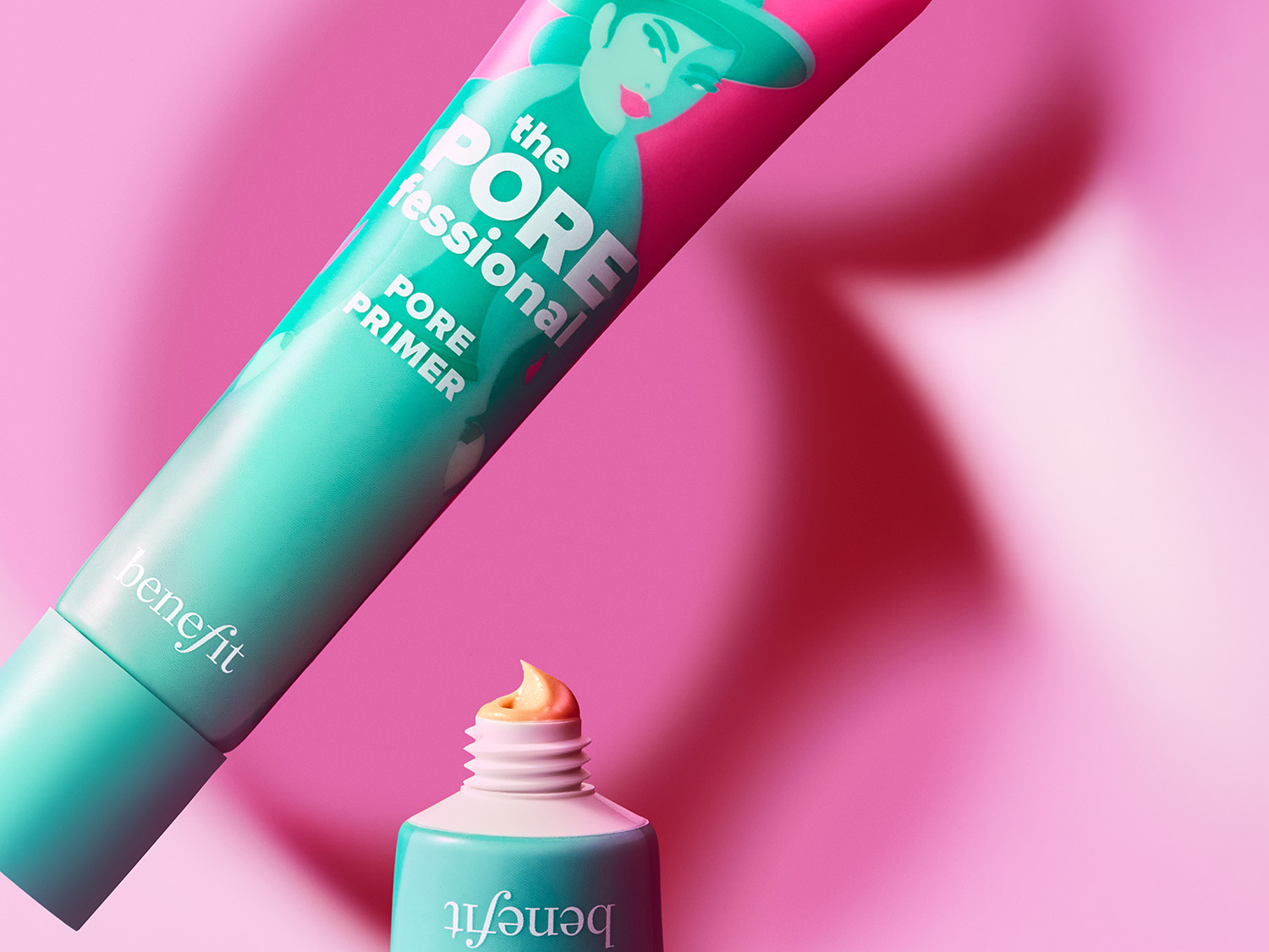Nahaufnahme von Benefit The POREfessional Pore Primer in einer türkisfarbenen Tube mit rosa Akzenten und einer kleinen Menge Primer, die aus der Öffnung quillt, vor einem rosa Hintergrund.