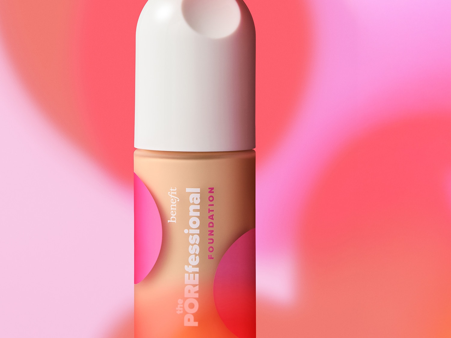 Benefit The POREfessional Foundation in einer hellbraunen Flasche mit weißem Deckel, verziert mit rosa Kreisen, vor einem verschwommenen rosa Hintergrund.