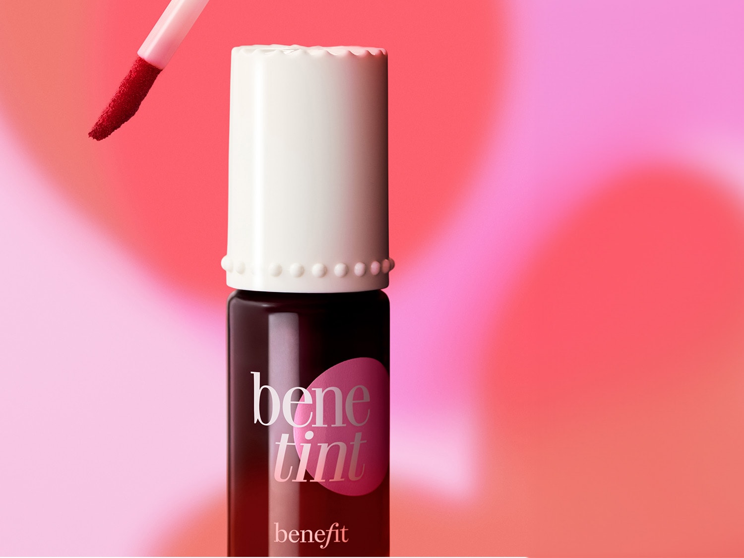 Nahaufnahme von Benefit Benetint Rosengetönter Lippen- und Wangenfärbung mit weißem Deckel und Applikator vor einem rosa Hintergrund.