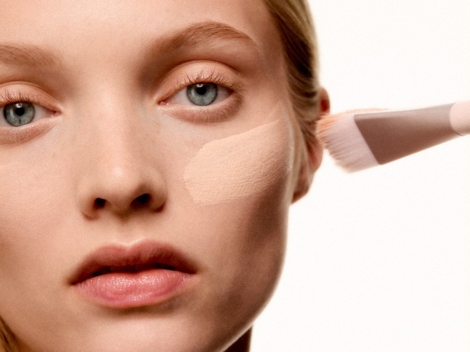 Gros plan d'une femme appliquant du fond de teint beige avec un pinceau, pour un teint uniforme et impeccable.