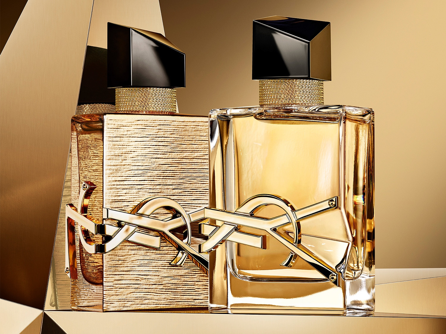 Dwa flakony perfum YSL w odcieniach złota, z charakterystycznym logo marki na pierwszym planie, emanujące luksusem i elegancją.