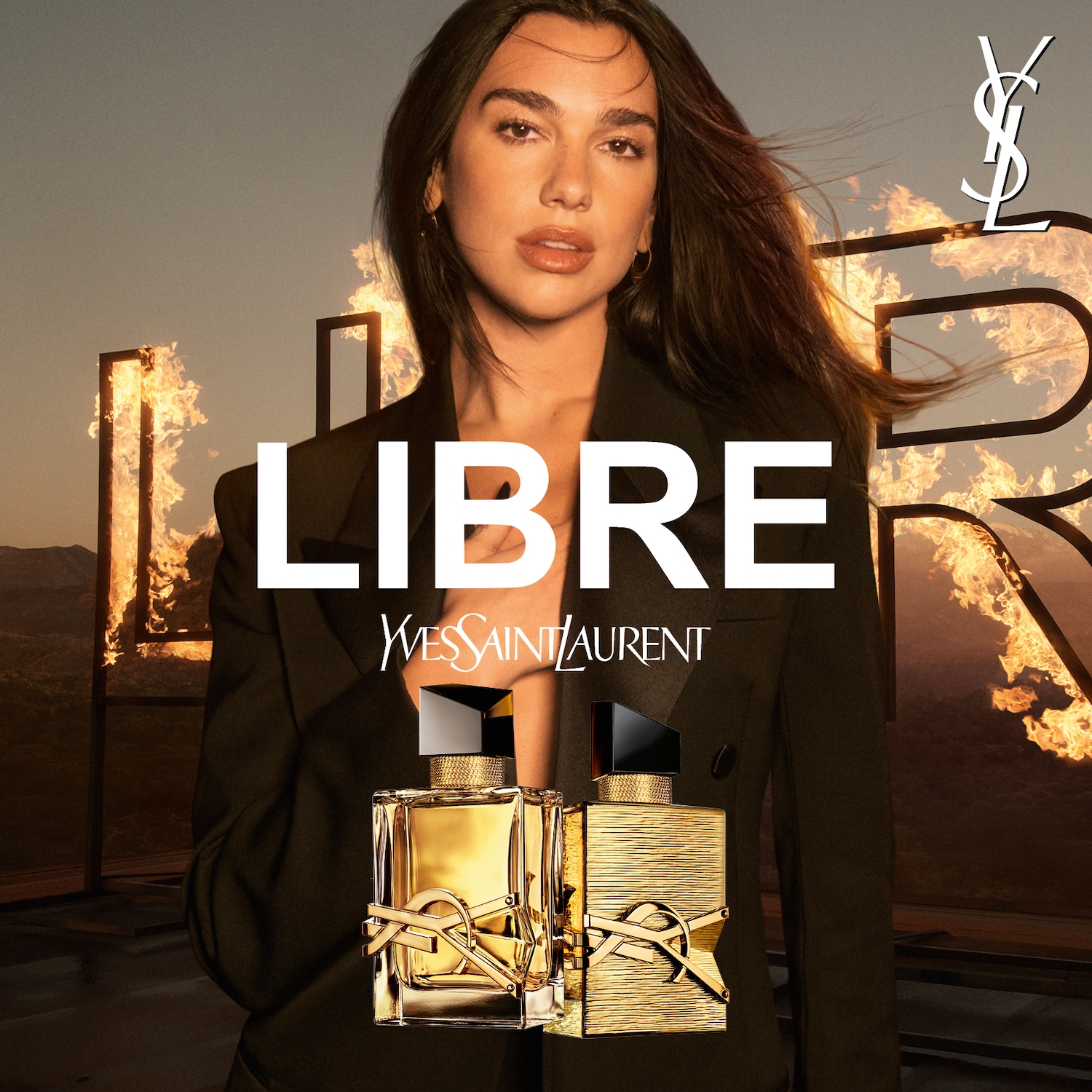 Na tle płomieni i pustynnego krajobrazu, Dua Lipa prezentuje zapach Yves Saint Laurent Libre w złotych flakonach, emanujący luksusem i nowoczesnością.