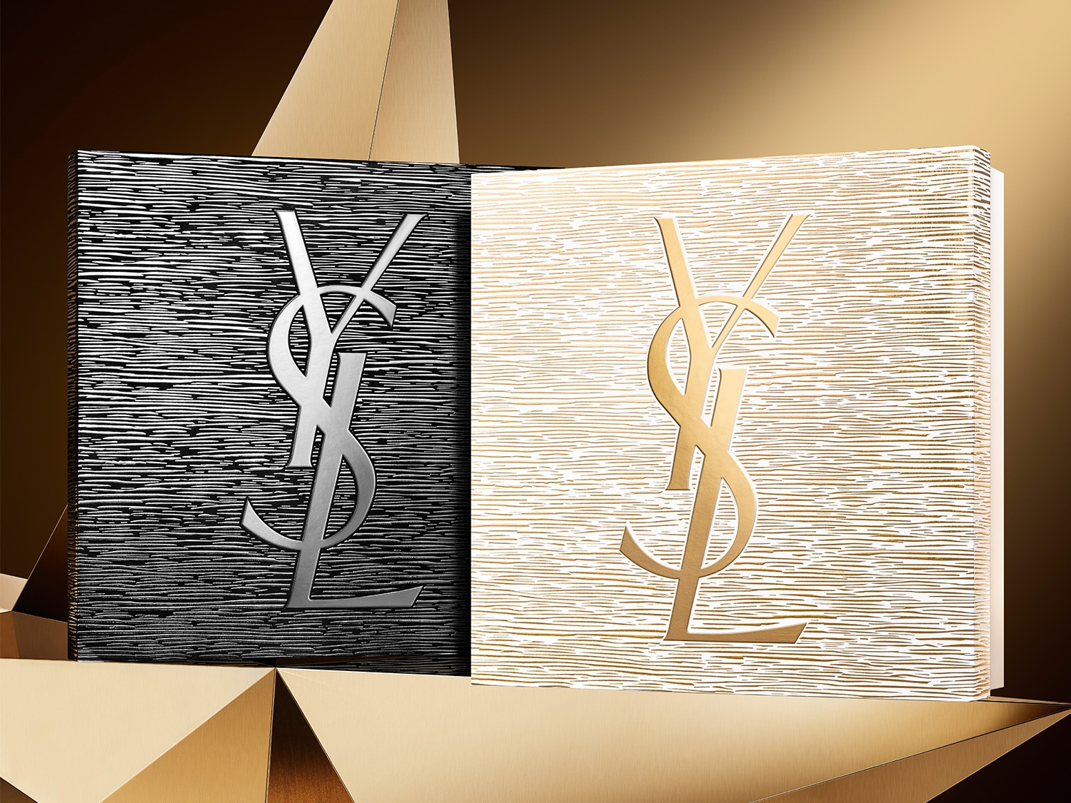 Dwa eleganckie pudełka YSL, jedno czarne ze srebrnym logo, drugie białe ze złotym logo, prezentowane na złotym tle.